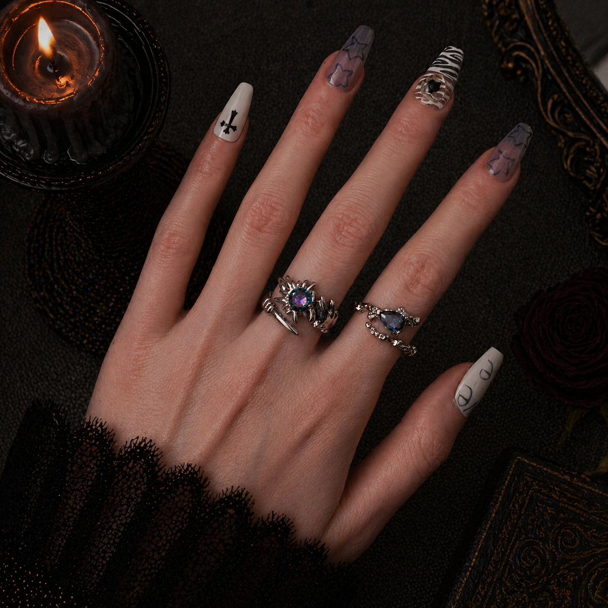Silver spiked claw ring with iridescent stone worn on middle finger and silver thorn teardrop ring on ring finger, dark gothic background with black candle