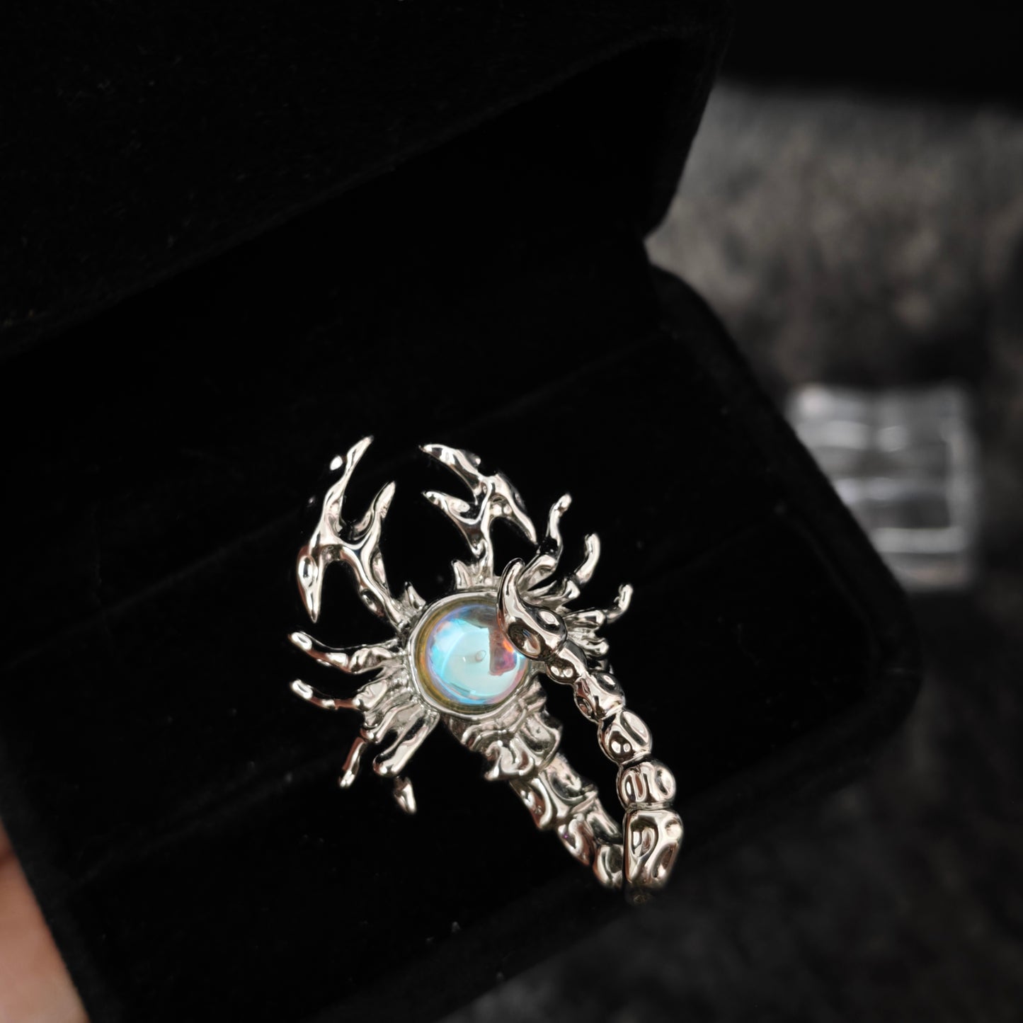 Celestial scorpion ring with iridescent stone detail in black velvet box, close-up side view
