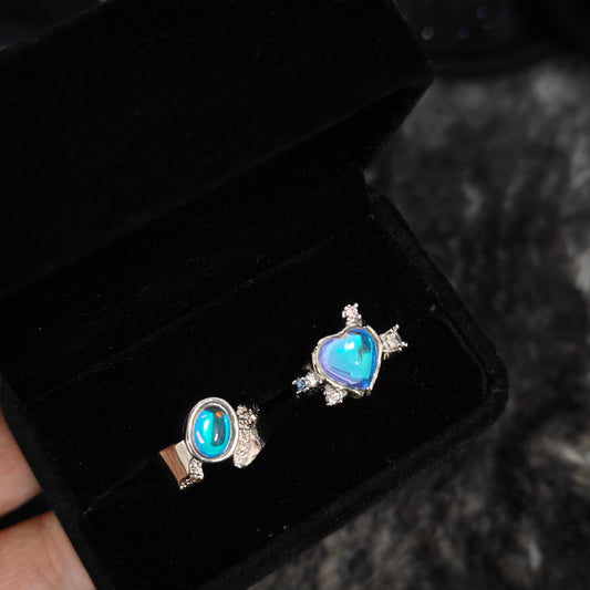 Two iridescent blue rings displayed side by side in black velvet box, overhead flat view