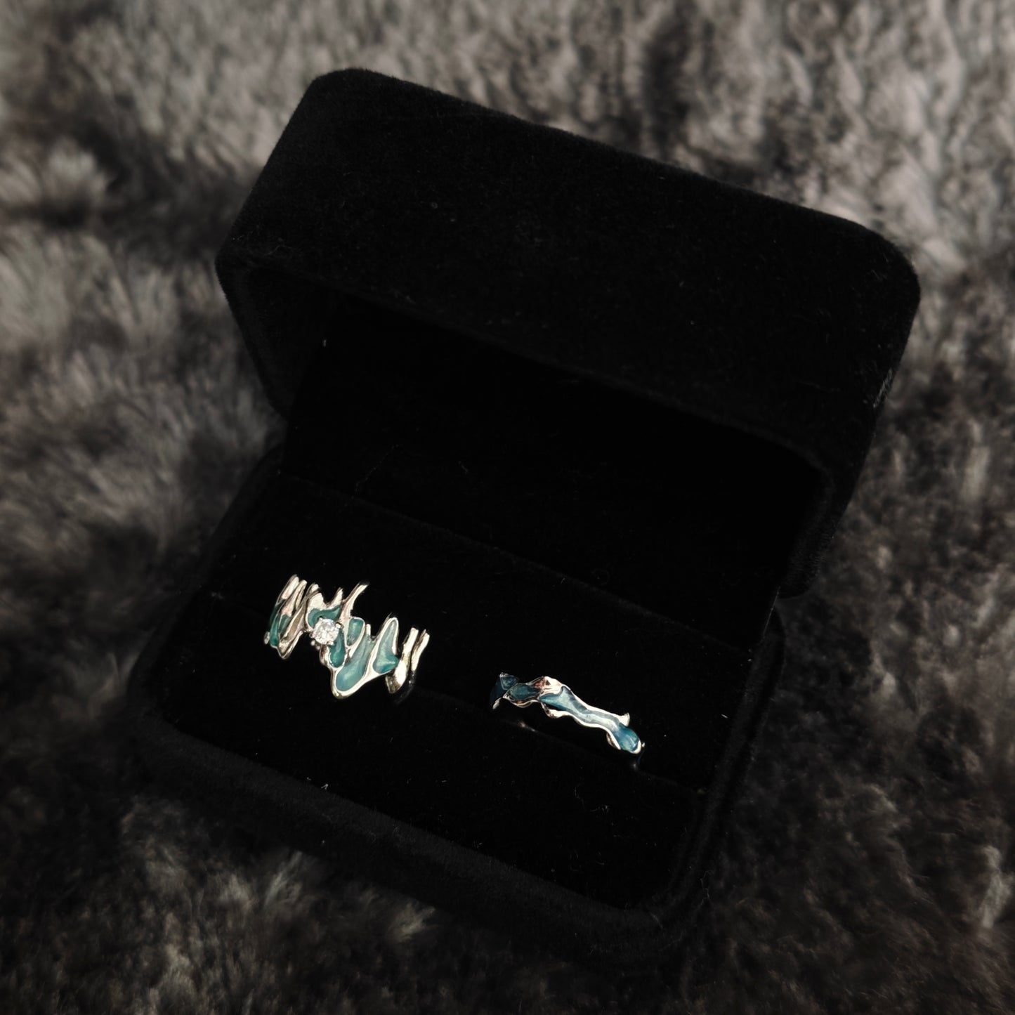 Teal enamel molten wide band ring and slim wavy band ring in black velvet box, close-up side view