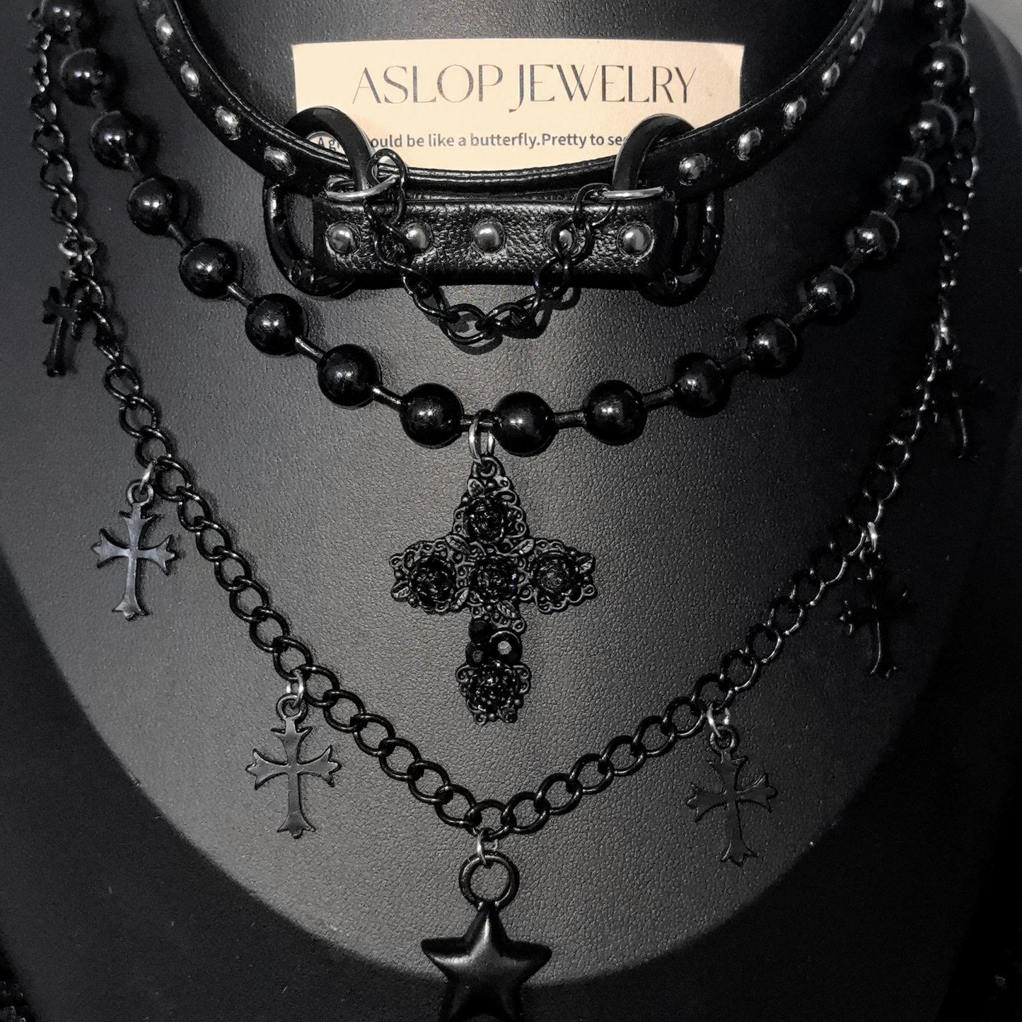 Black beaded necklace with cross and star pendants on a mannequin bust, branded 'Aslop Jewelry'.
