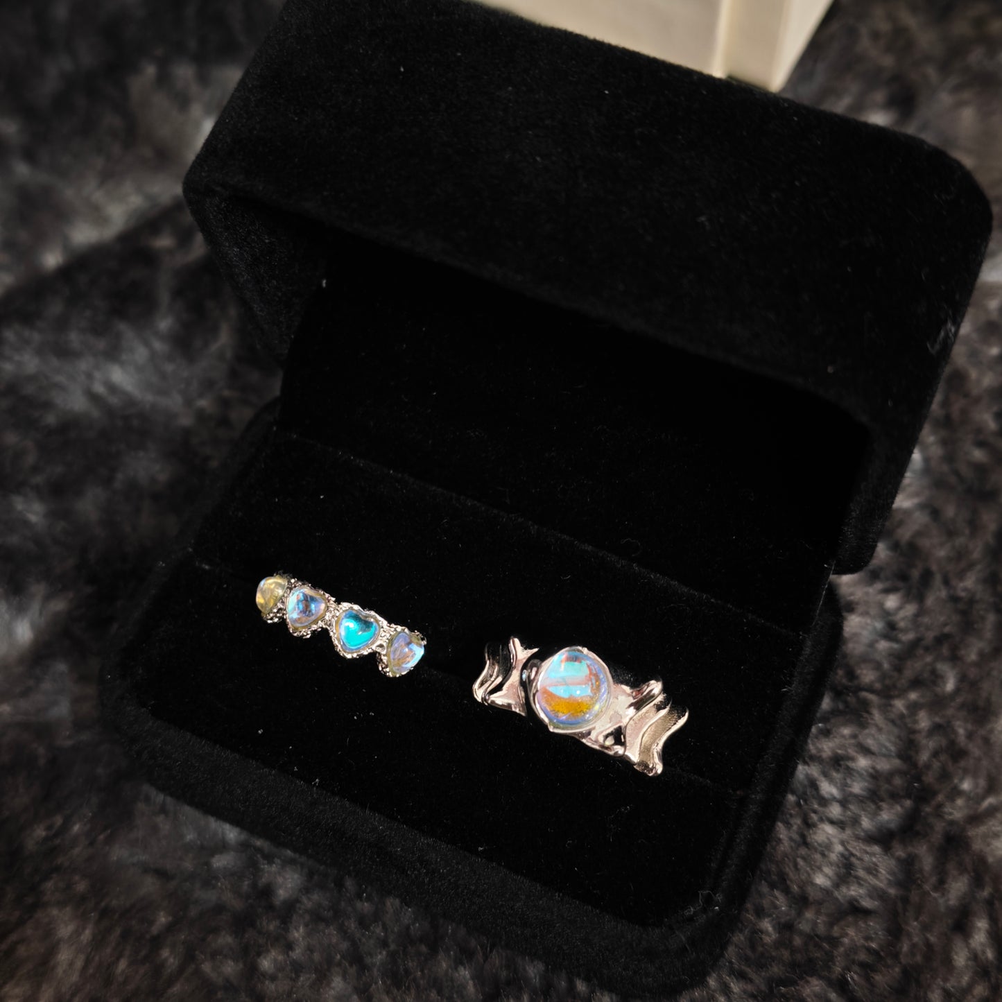 Triple heart aurora band and wavy oval stone wide band ring in open black velvet jewelry box, angled view