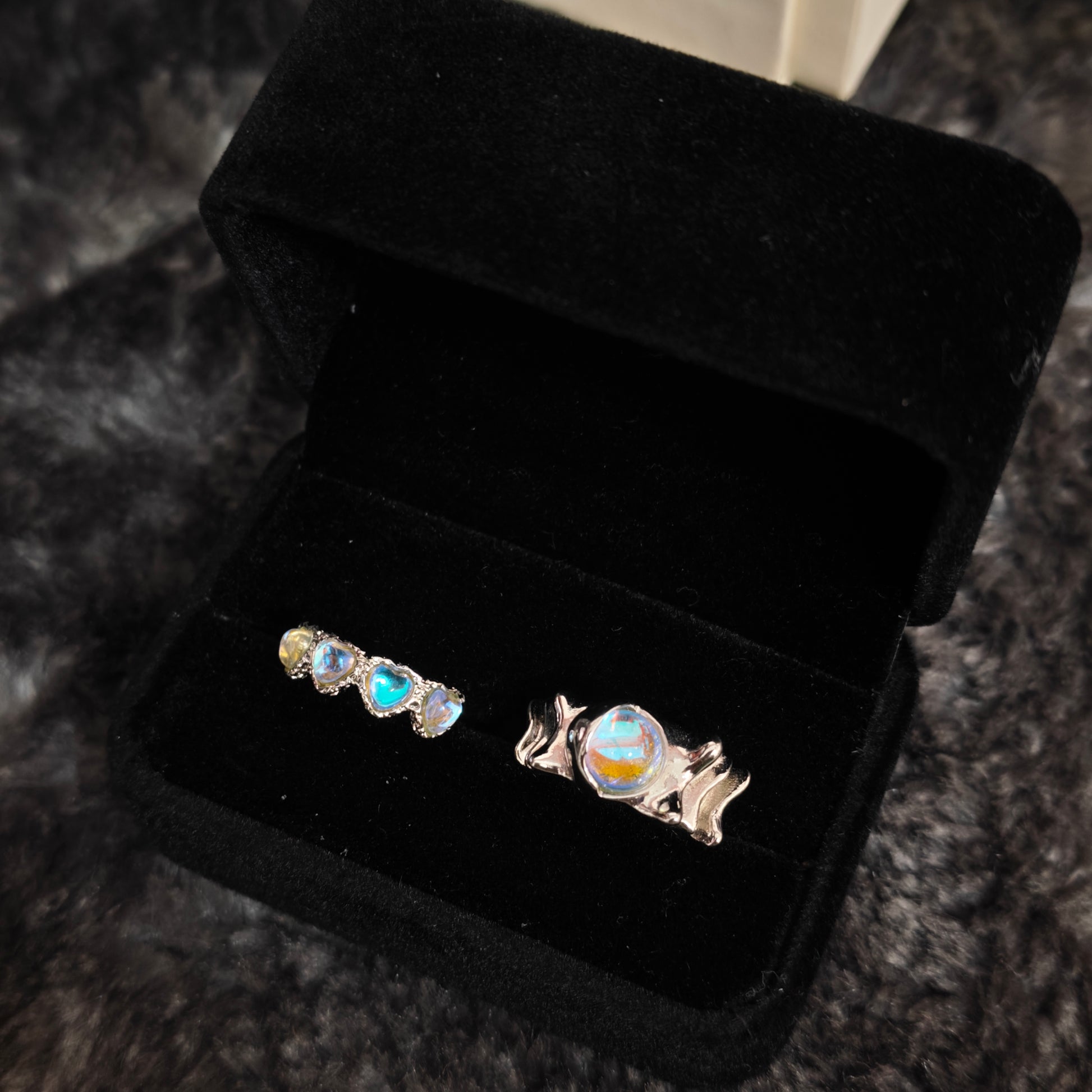 Triple heart aurora band and wavy oval stone wide band ring in open black velvet jewelry box, angled view