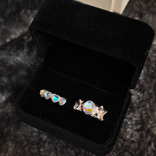 Triple heart aurora band and wavy oval stone wide band ring in open black velvet jewelry box, angled view