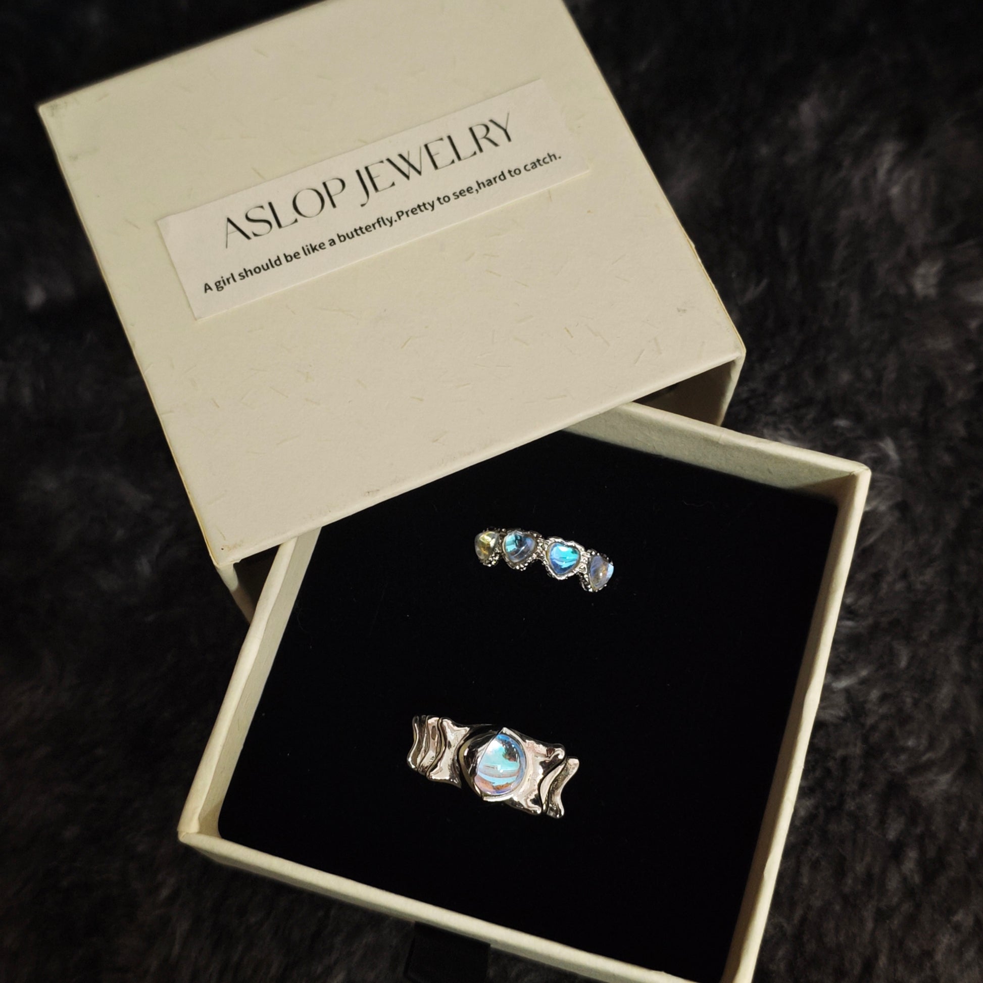 Triple heart aurora ring and wavy oval band ring in open Aslop Jewelry white gift box, angled view