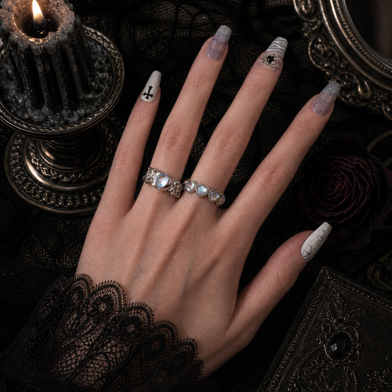 Iridescent triple heart band ring and aurora oval wavy wide band ring worn together on hand, dark gothic candle background
