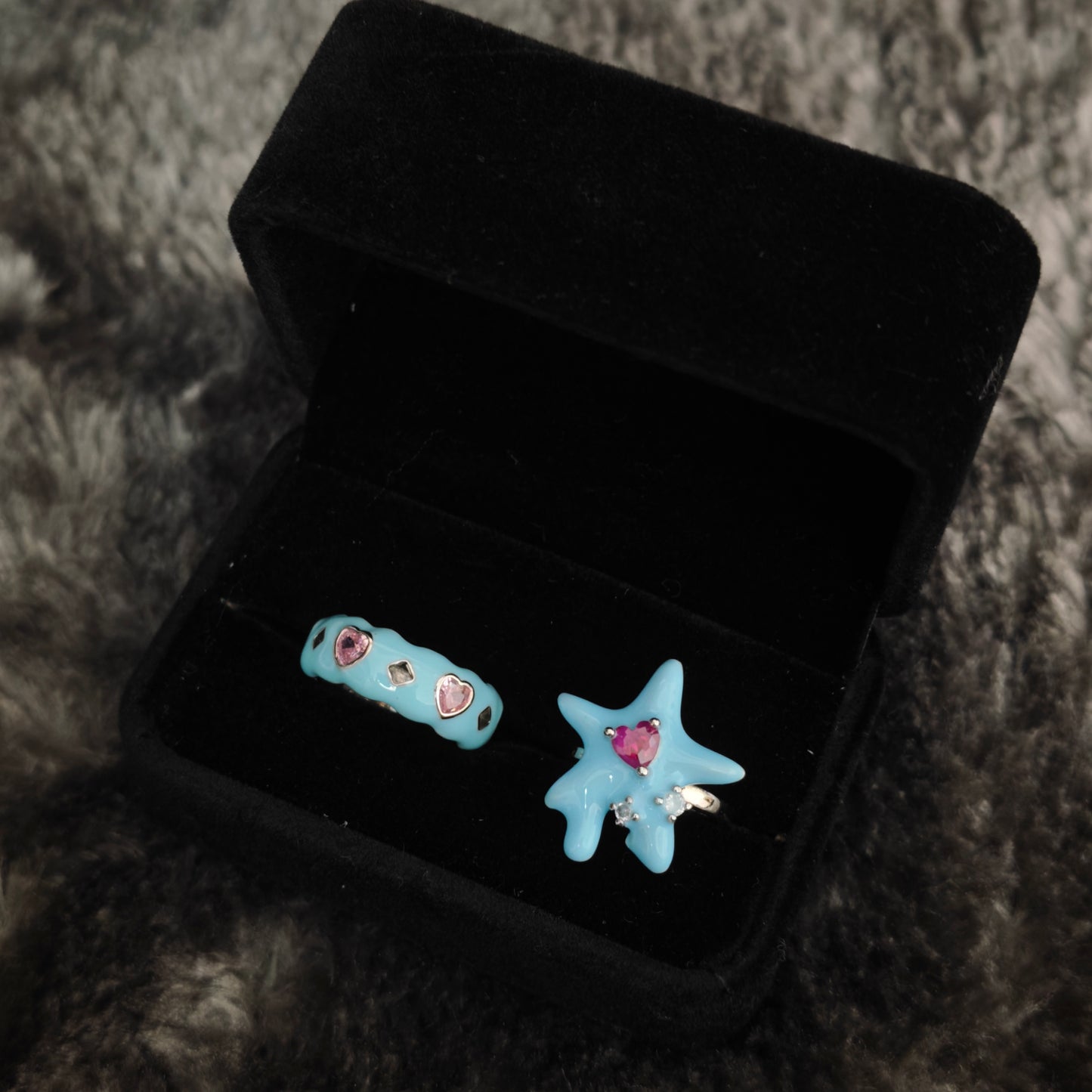 Baby blue enamel star ring and heart gem band ring displayed in open black velvet jewelry box, angled overhead view