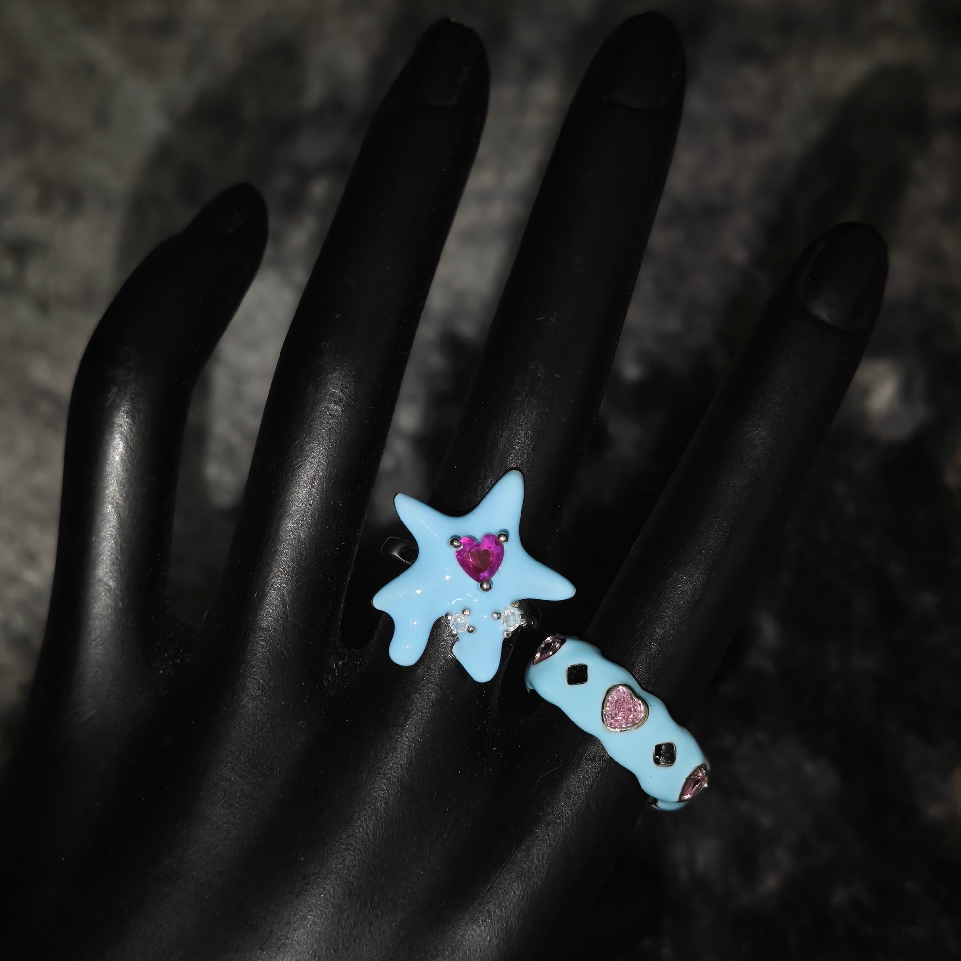 Star-shaped blue rings with pink heart stones on a dark background