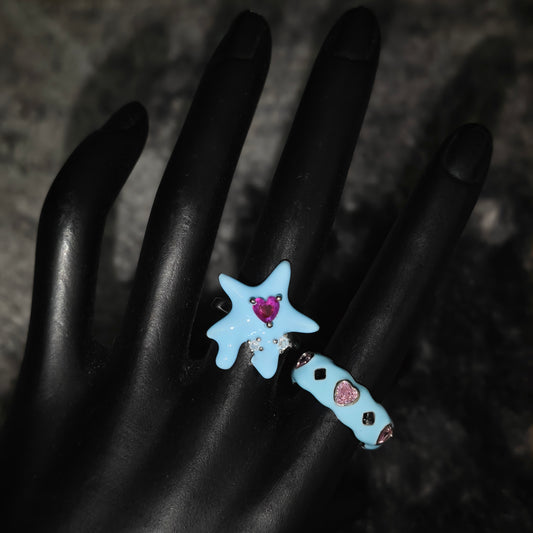 Star-shaped blue rings with pink heart stones on a dark background