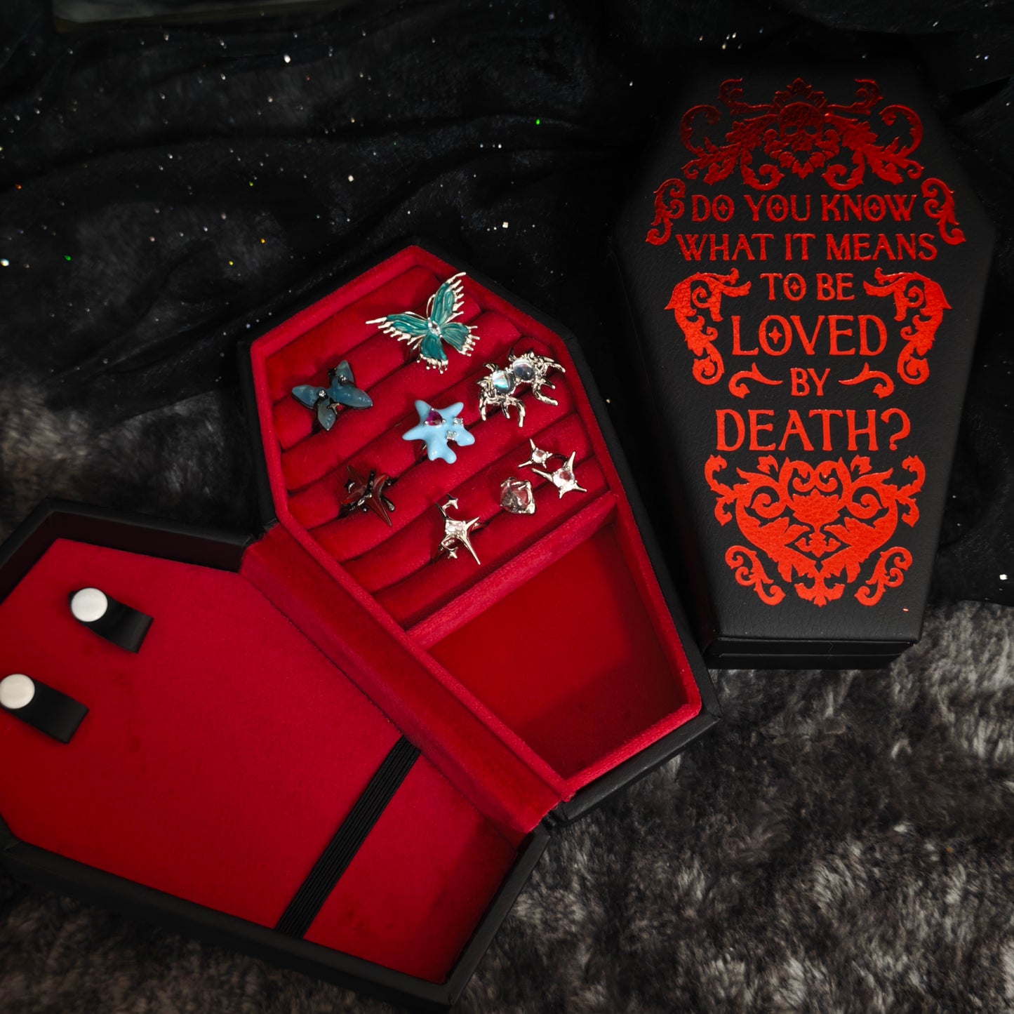 Gothic coffin jewelry box open with rings and earrings stored inside red velvet slots, styled with gothic coffin lid