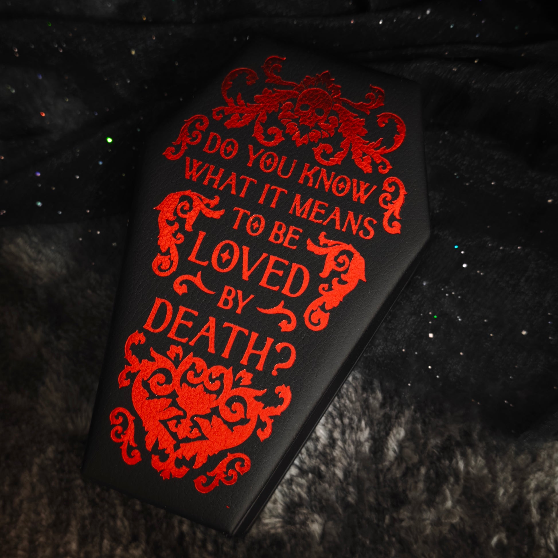 Black coffin jewelry box with red foil gothic text "Do You Know What It Means To Be Loved By Death" close-up front view