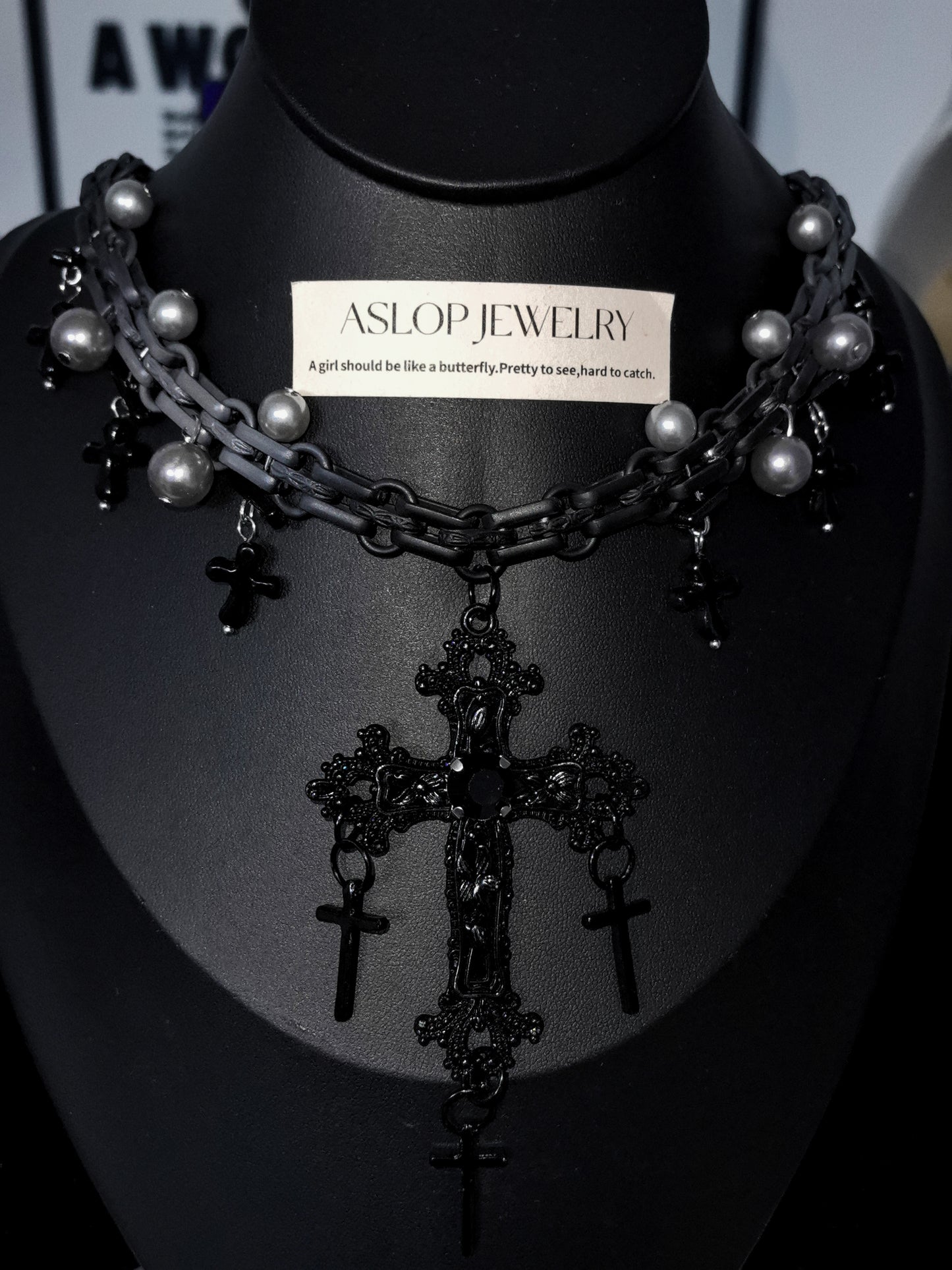 Black and grey necklace with crosses on a mannequin bust, branded 'Aslop Jewelry'.