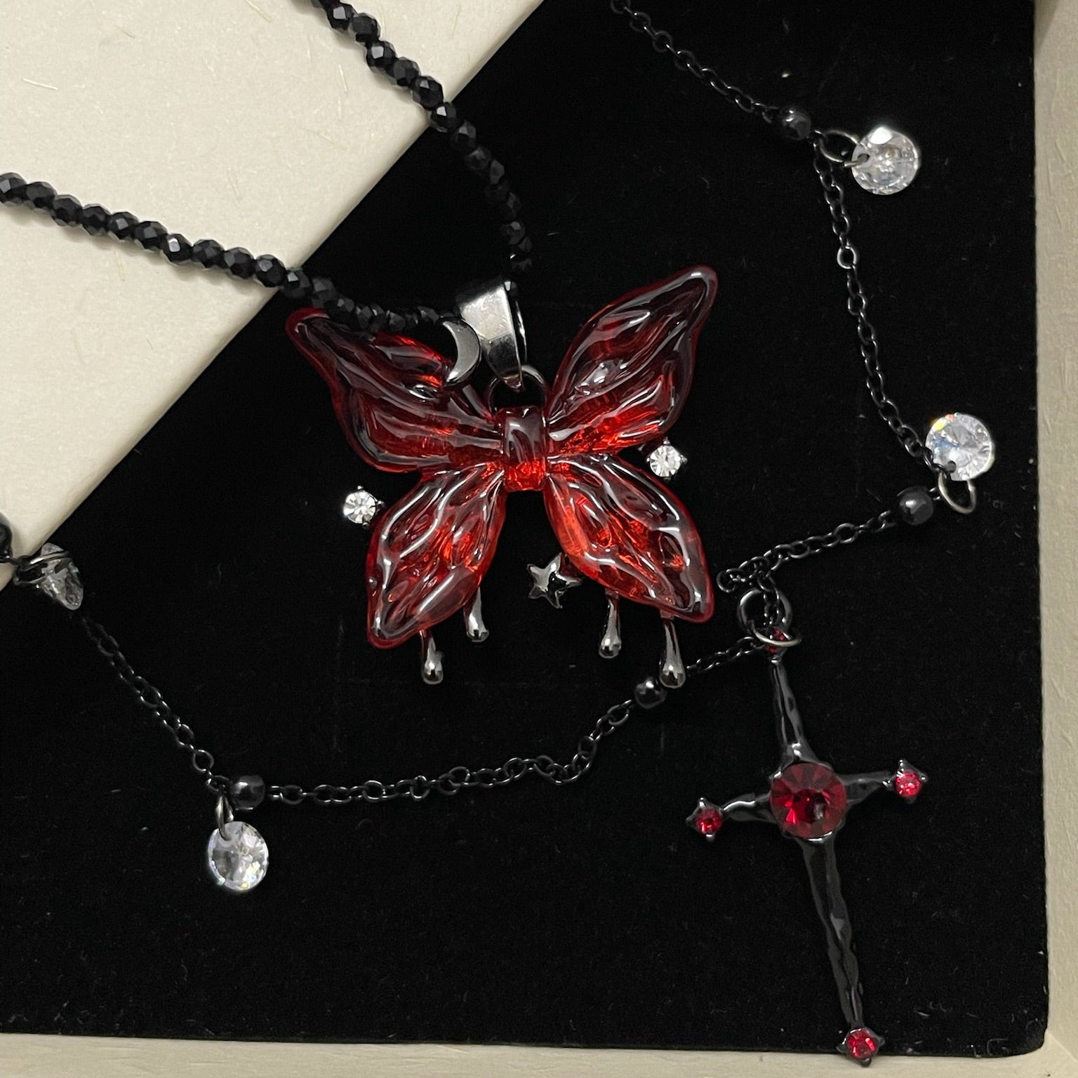 Blood Rose Butterfly & Gothic Cross Necklace in open black velvet jewelry box, angled view