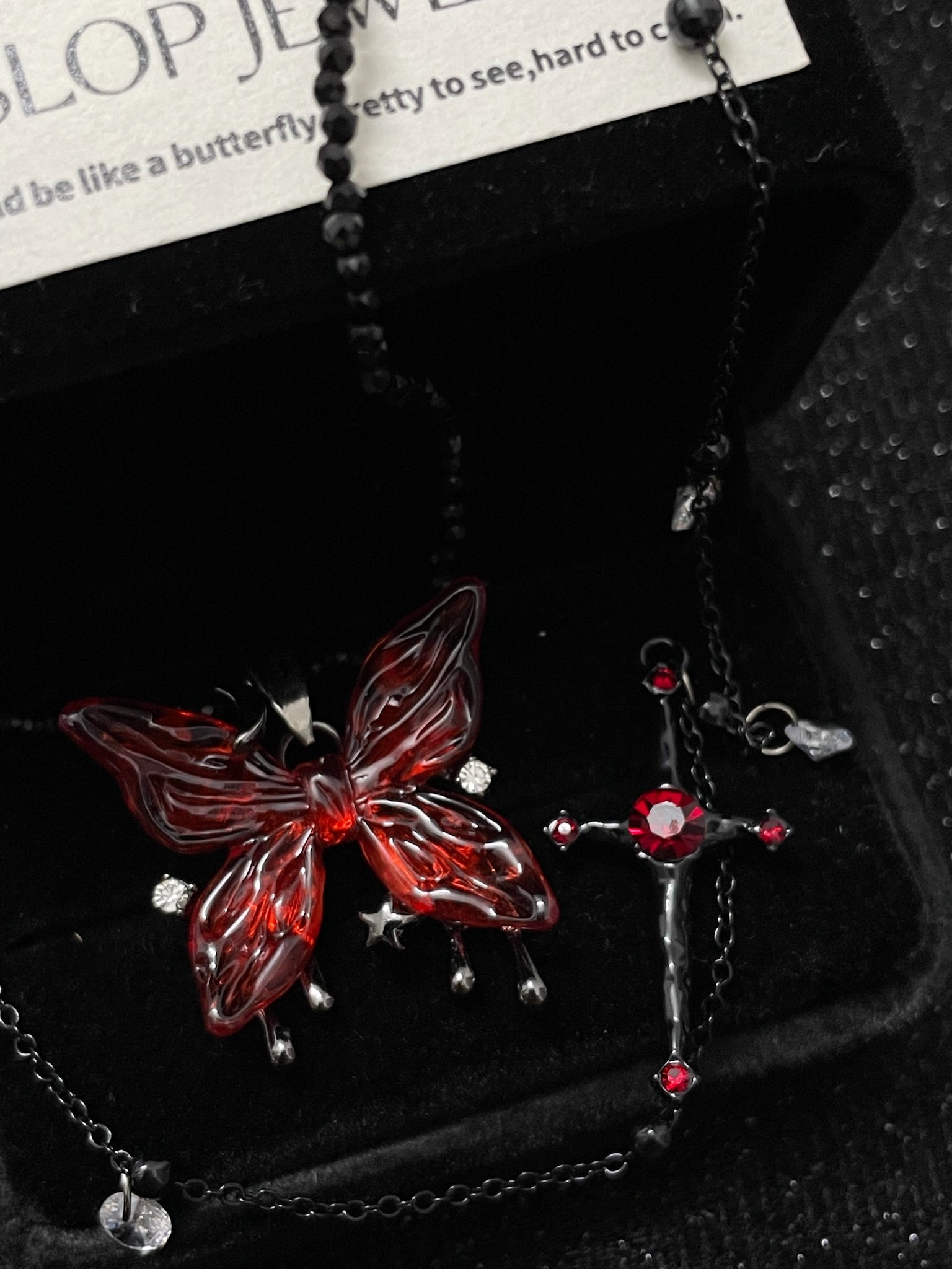 Blood Rose Butterfly & Gothic Cross Necklace in open black velvet jewelry box, overhead flat lay