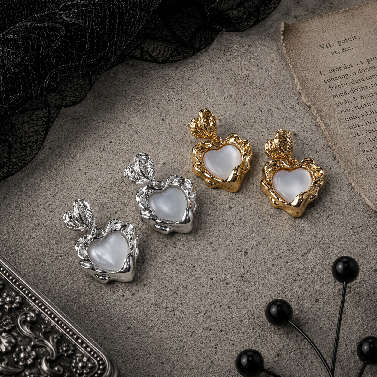 Silver and gold baroque sacred heart pearl drop stud earrings displayed side by side on grey stone surface, both colourways