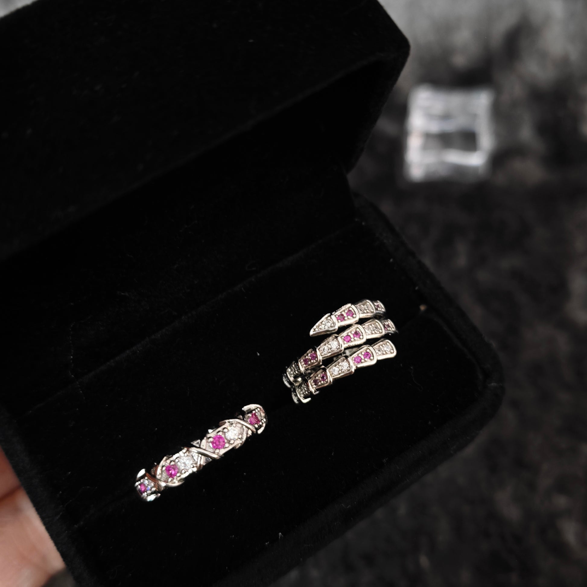 Serpent wrap ring and pavé band with pink and clear stones in black velvet box, close-up side view