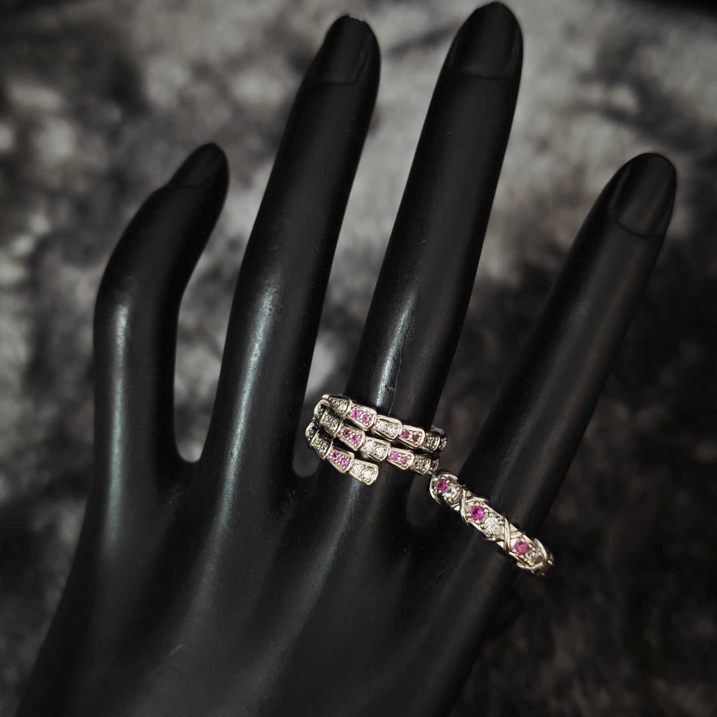 Silver three-coil serpent wrap ring with pink and clear stones on black mannequin hand, detail view