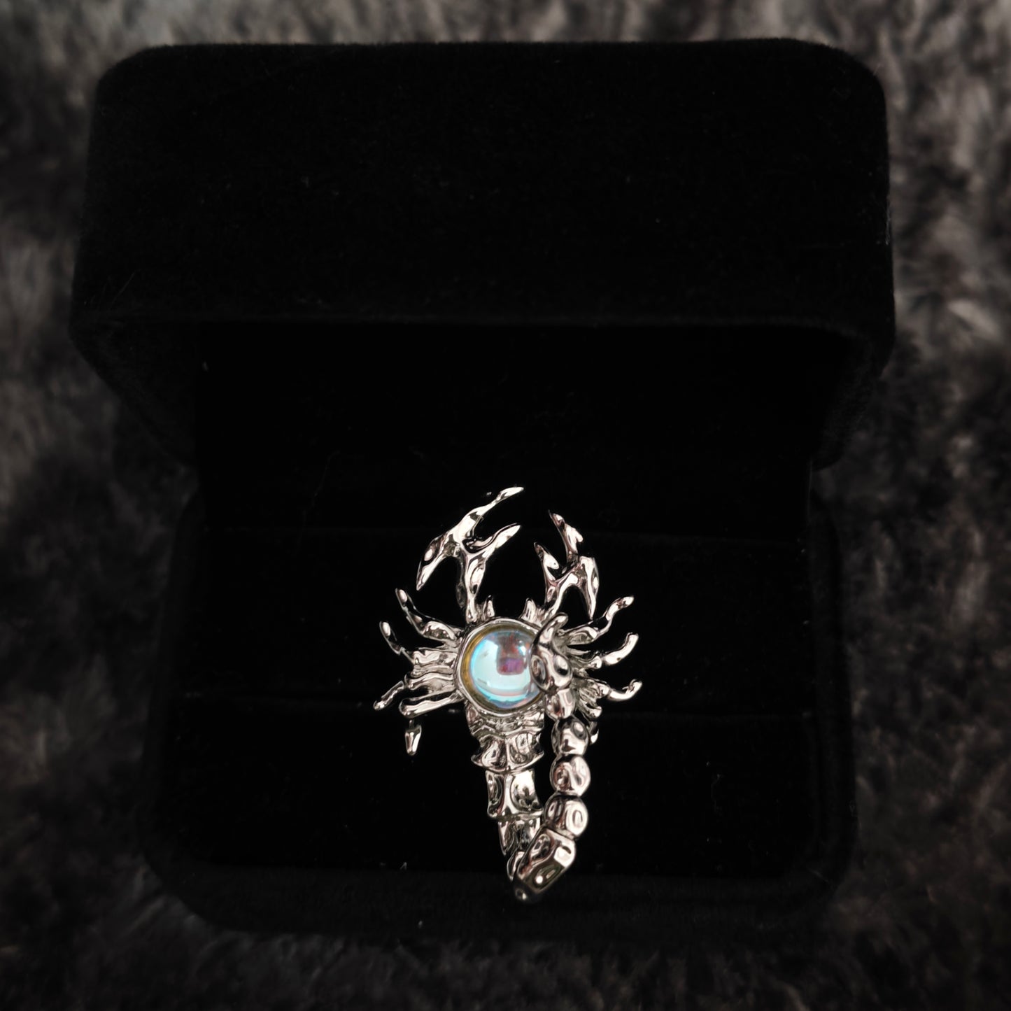 Silver scorpion ring with aurora stone in open black velvet box, overhead flat view