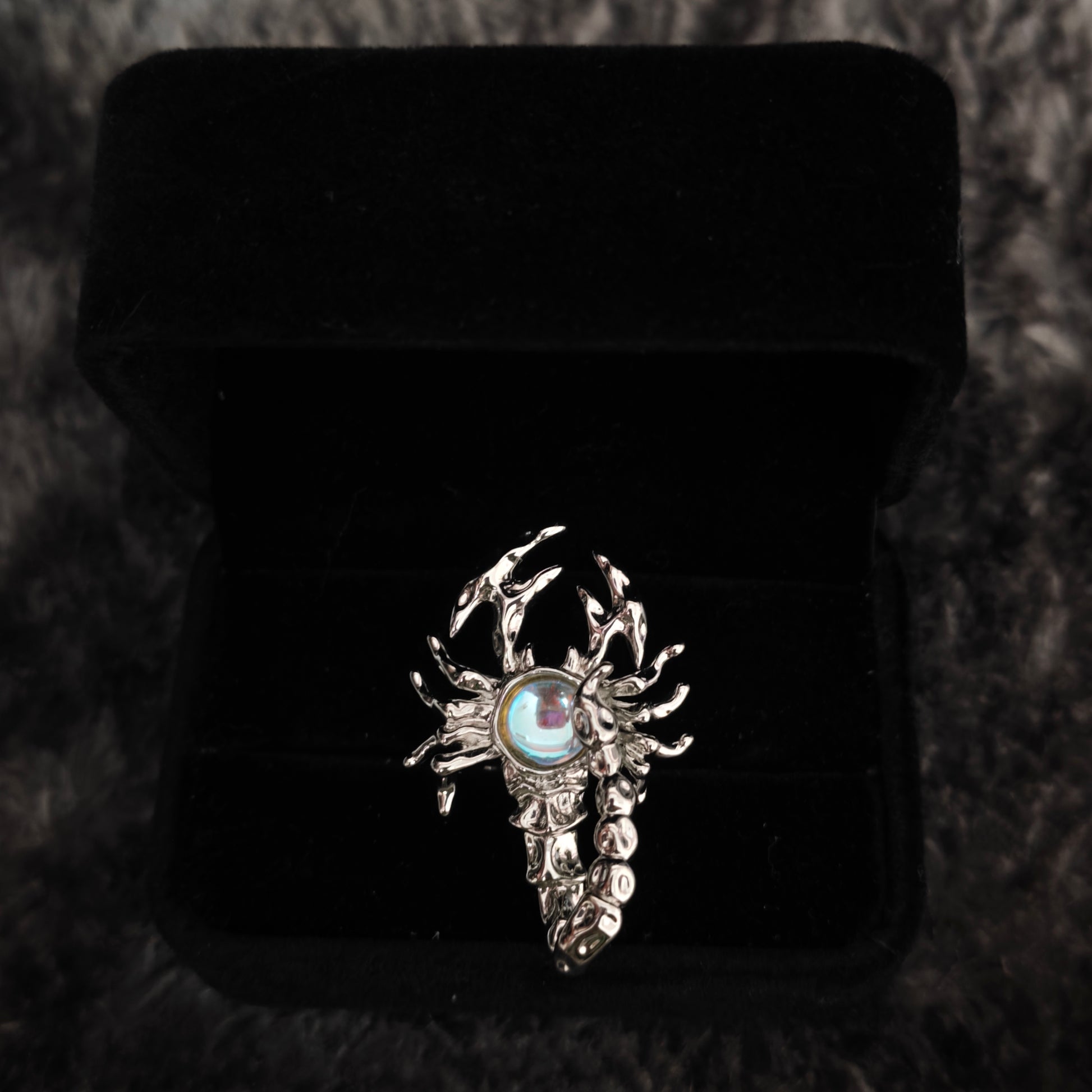 Silver scorpion ring with aurora stone in open black velvet box, overhead flat view