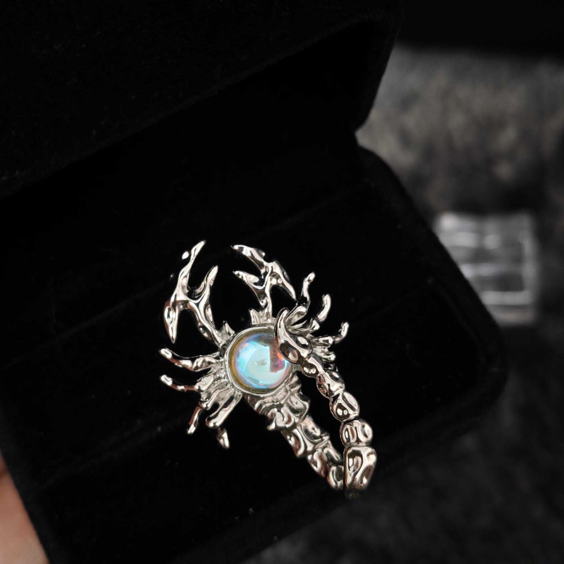 Celestial scorpion ring with iridescent stone detail in black velvet box, close-up side view