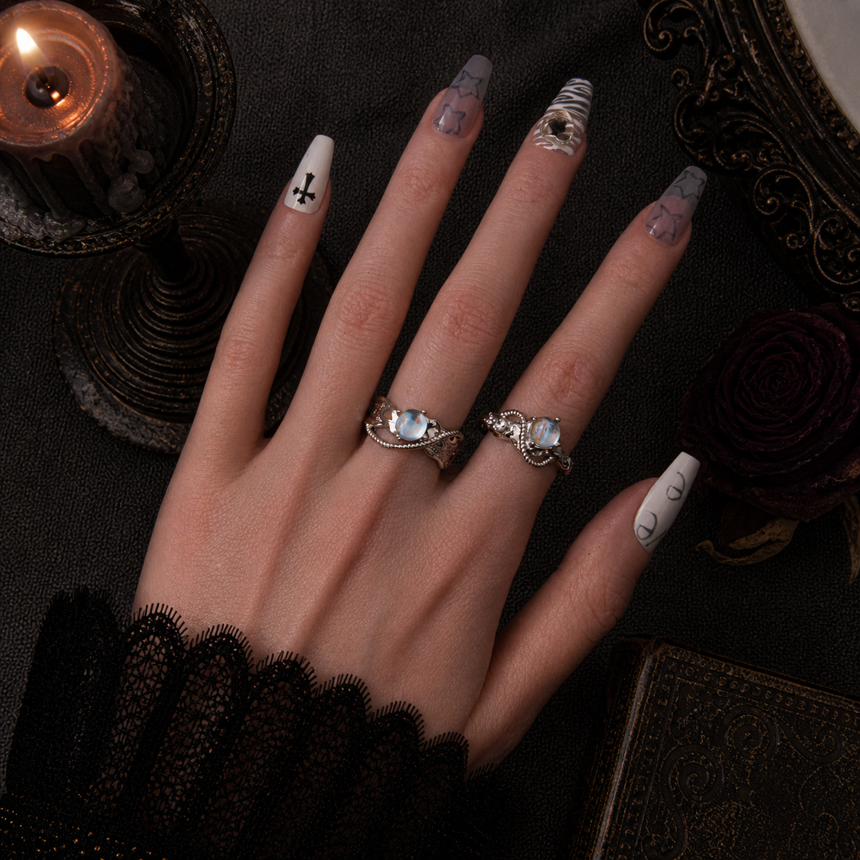 Two silver arc rings with iridescent stone worn on hand, dark gothic candle background