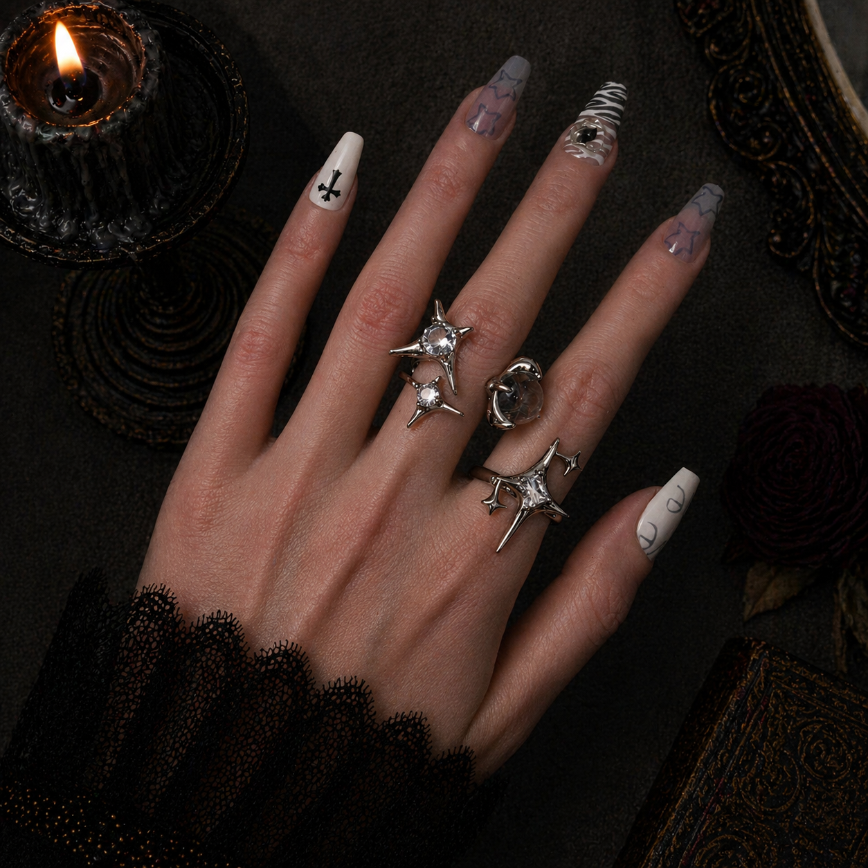 Two silver four-pointed star spike rings with clear stones worn stacked on hand, dark gothic candle background