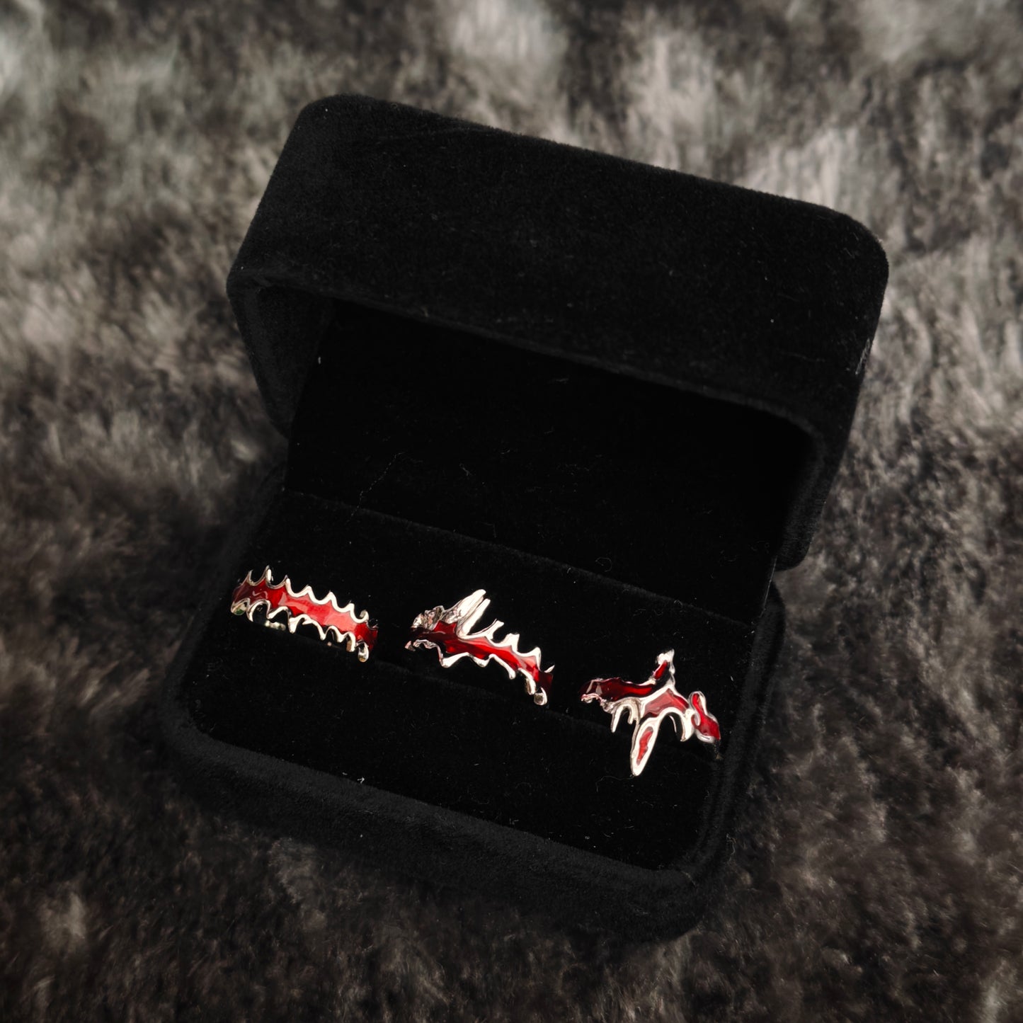 Three red enamel vampire fang and blood drip rings in black velvet jewelry box, close-up side view