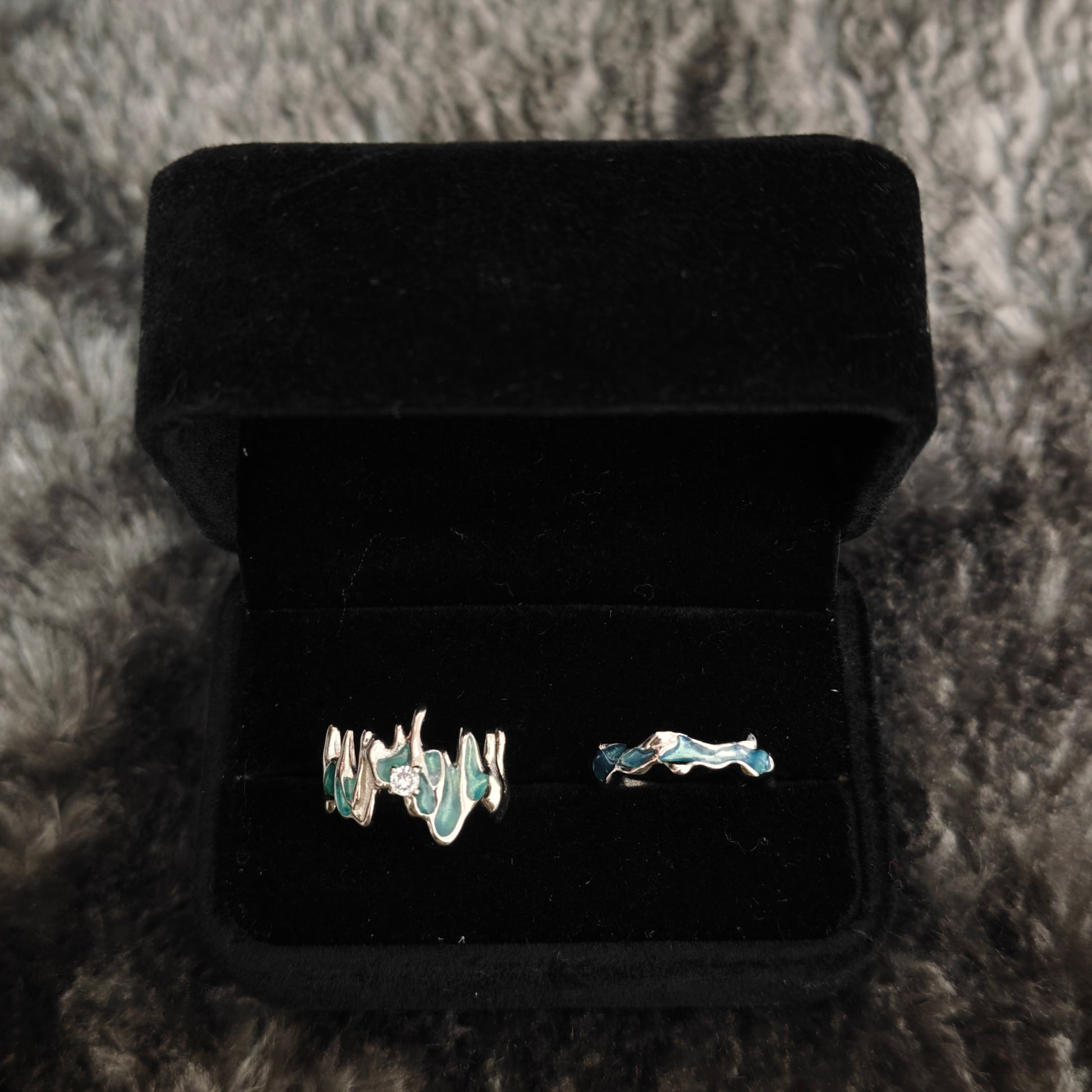 Two teal enamel stacking rings in open black velvet box, overhead flat view