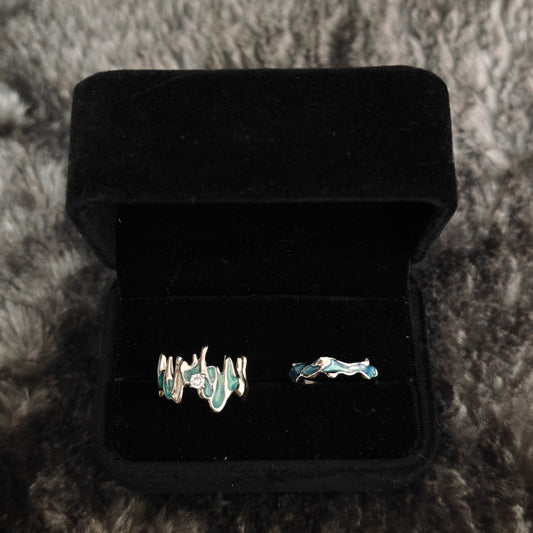 Two teal enamel stacking rings in open black velvet box, overhead flat view