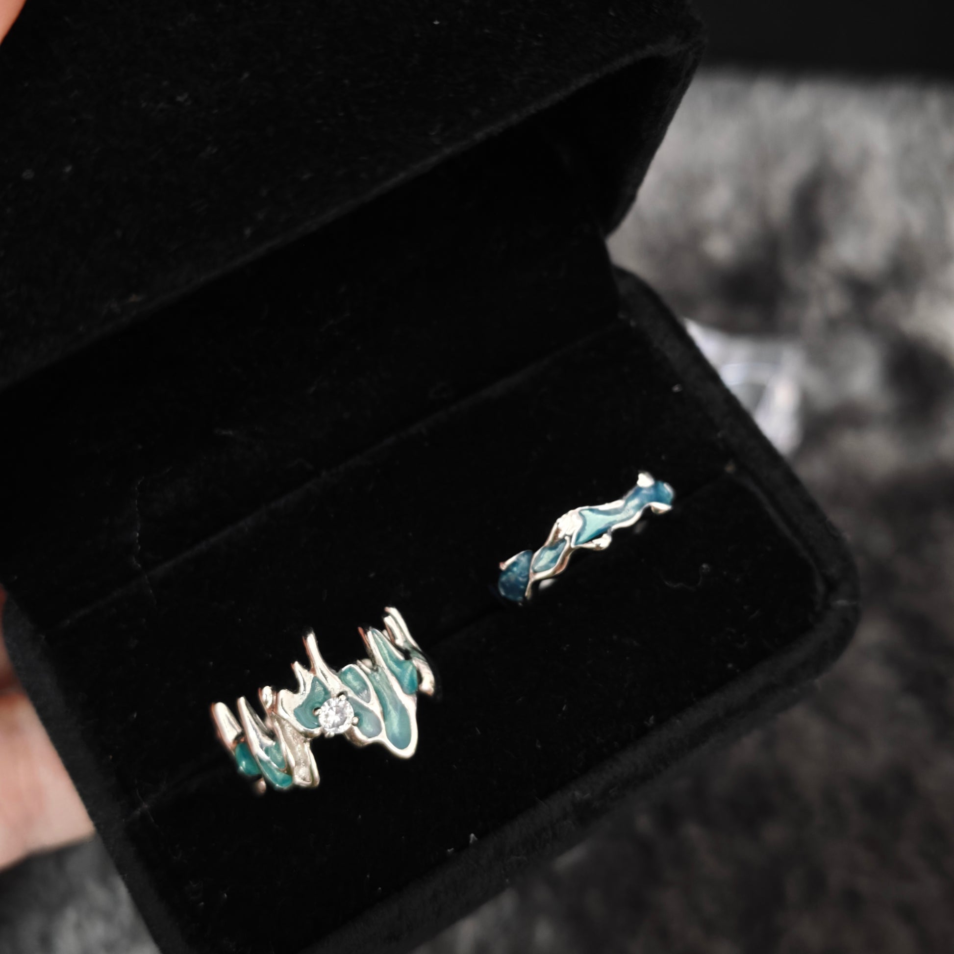 Two teal enamel stacking rings in open black velvet box, overhead flat view