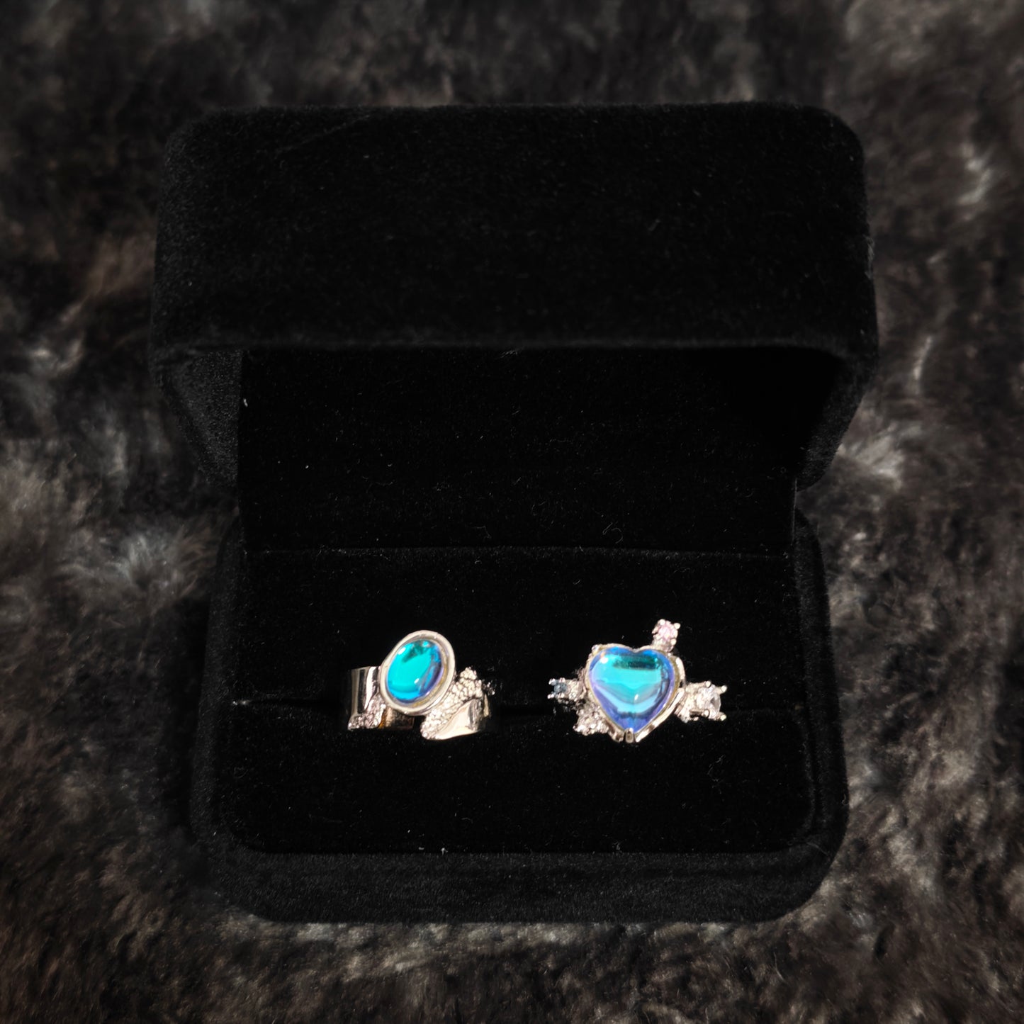 Blue aurora heart ring and wide oval band ring in open black velvet box, overhead flat view