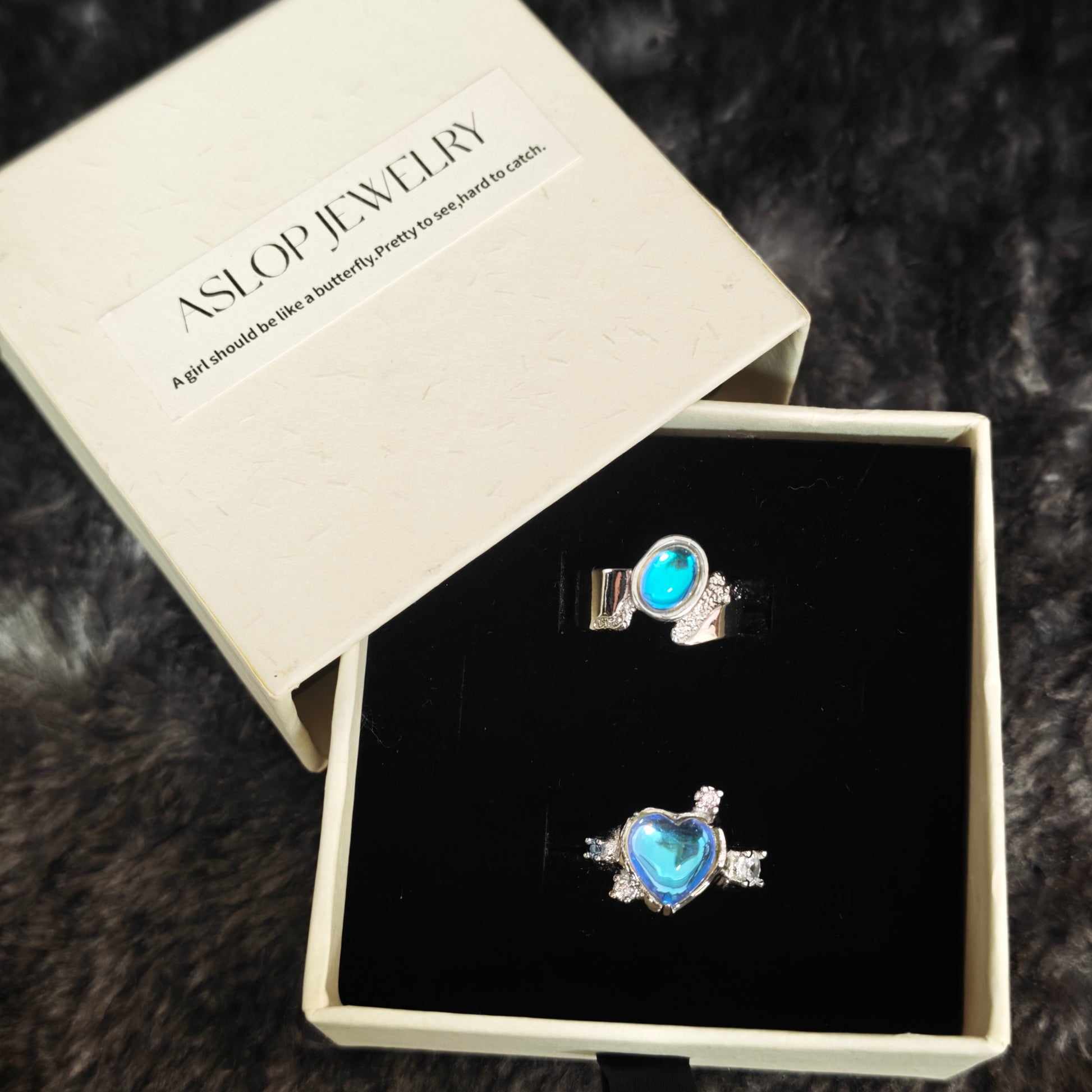 Blue aura ring set in open Aslop Jewelry white gift box showing heart ring and oval band ring, angled view