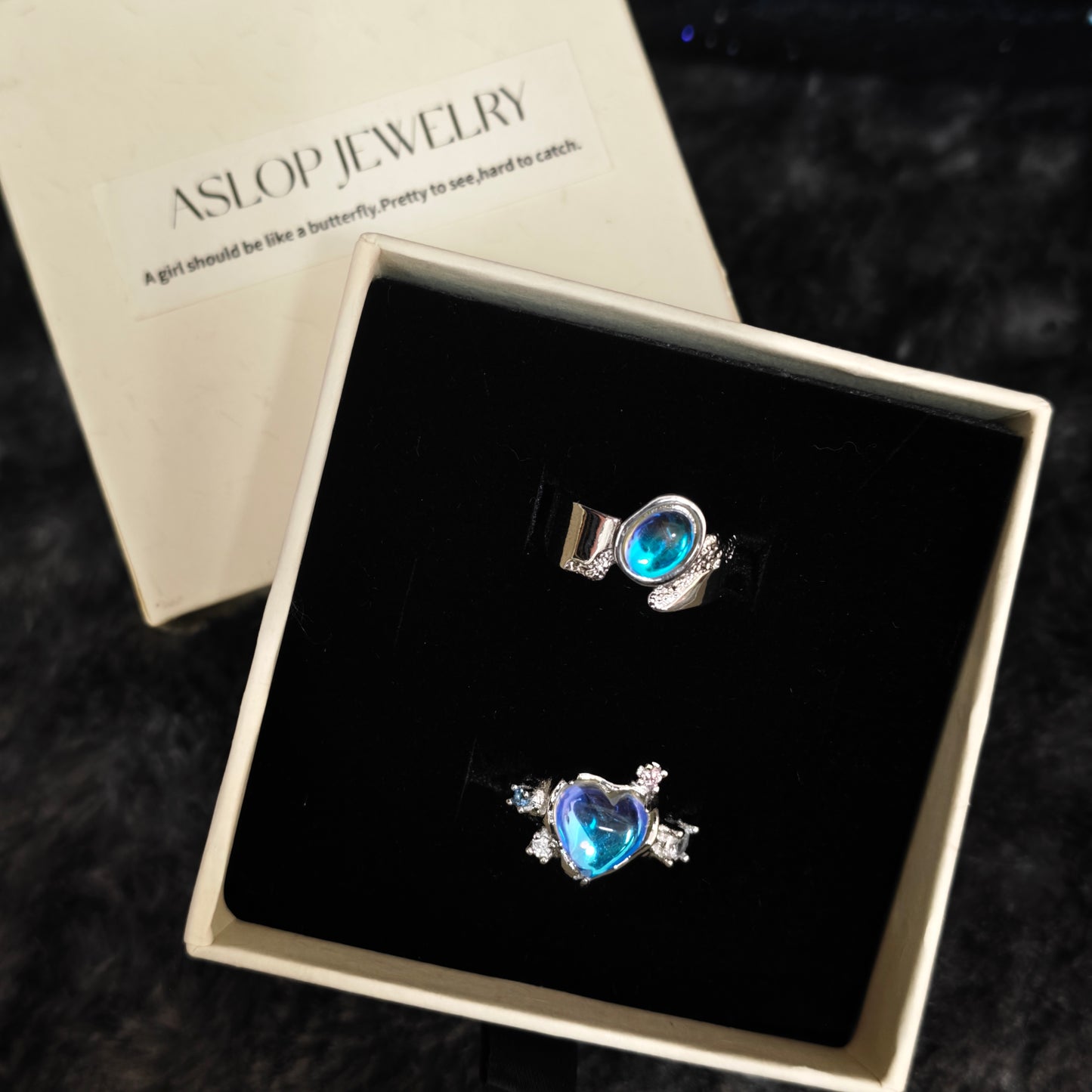 Blue aura heart ring and oval band ring in open Aslop Jewelry white gift box, overhead flat view