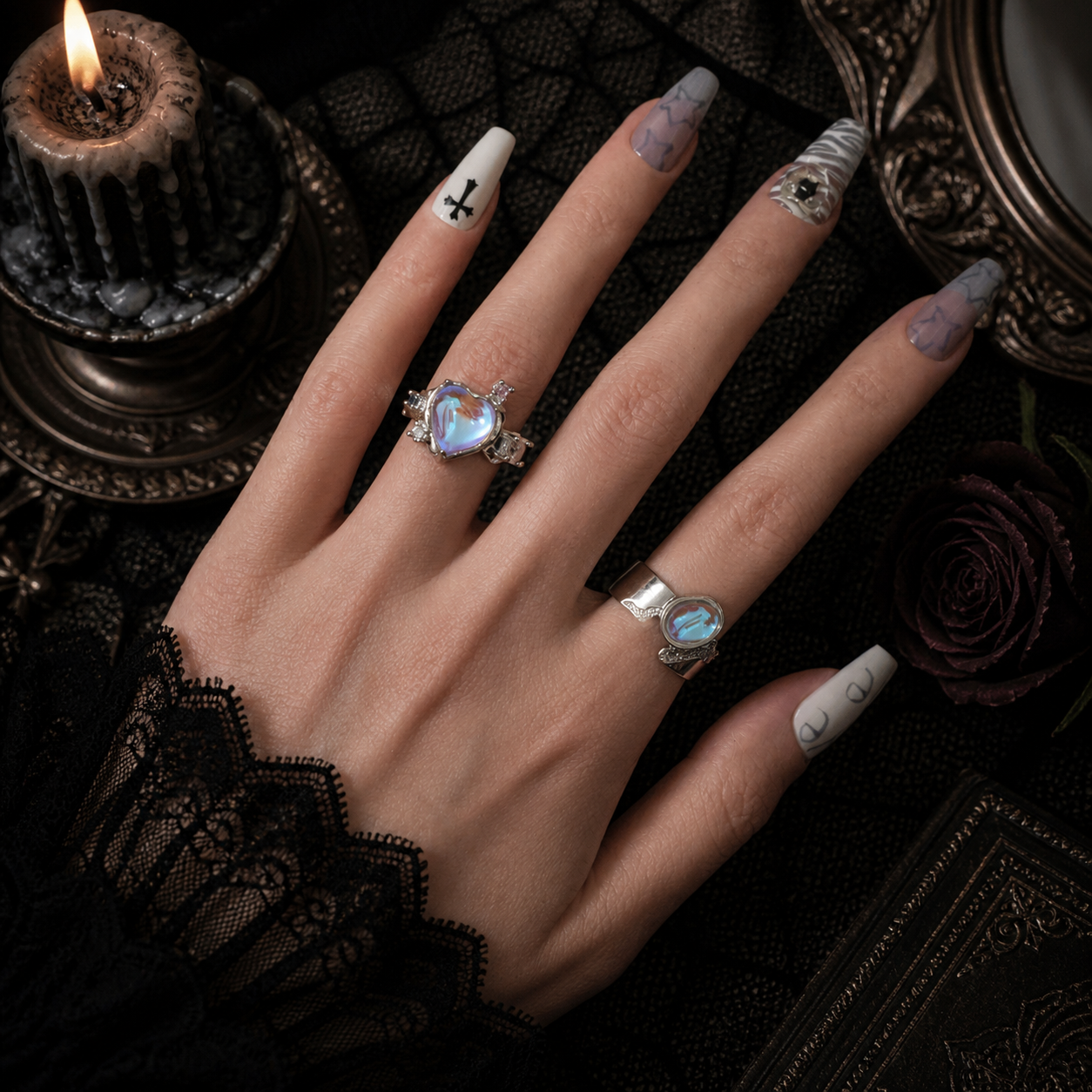 Iridescent blue heart ring and blue oval wide band ring worn together on hand, dark gothic candle background