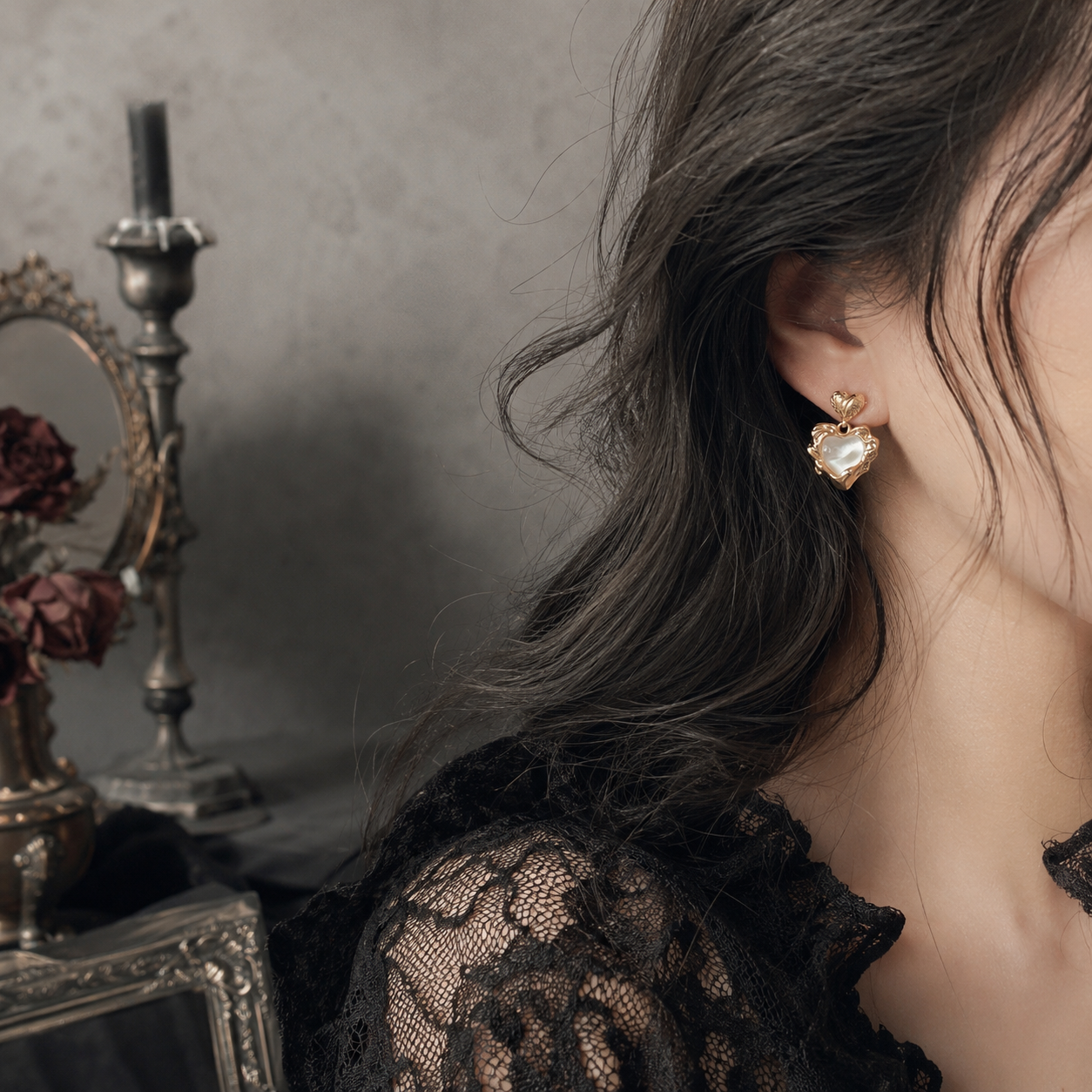 Gold sacred heart pearl drop stud earrings worn on ear, gothic dark vanity background with candelabra and dried roses