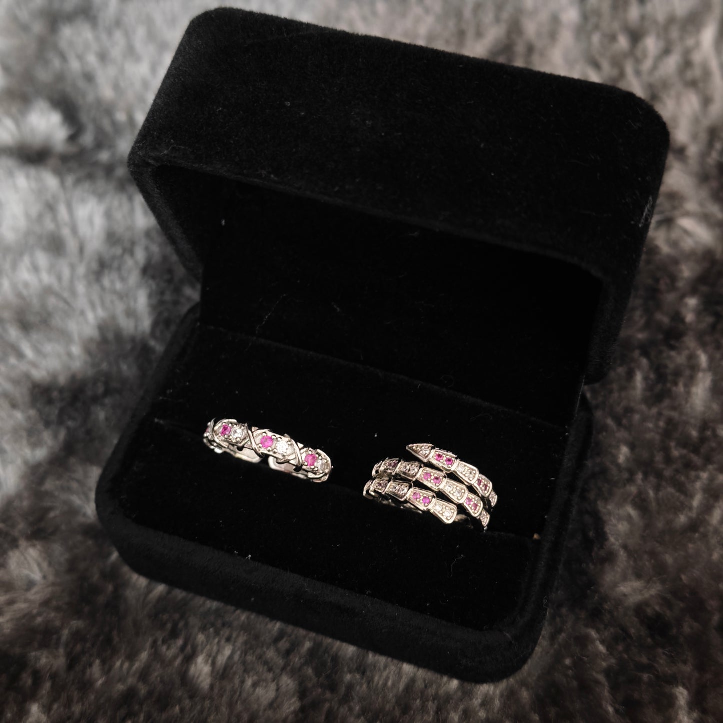 Silver three-coil serpent wrap ring with pink stones and pavé band ring in open black velvet box, angled view