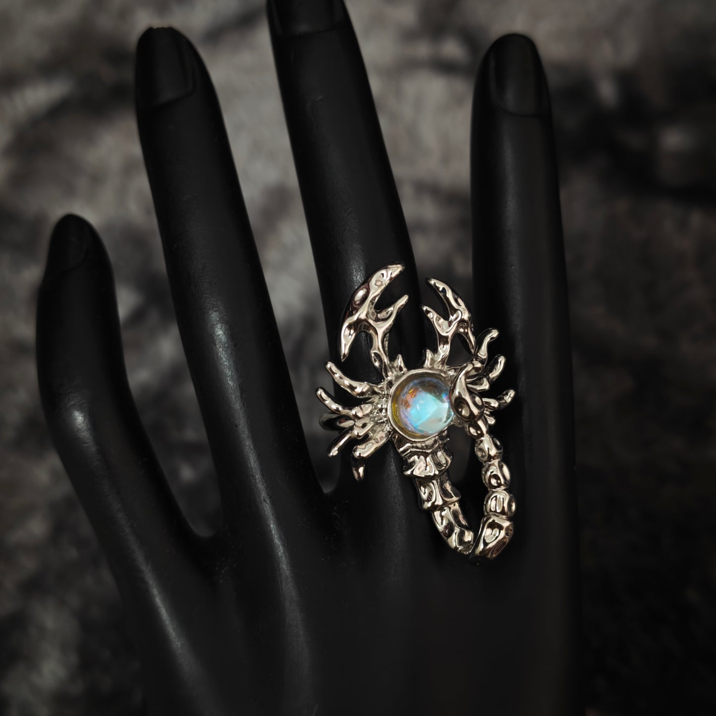 Silver scorpion ring with aurora iridescent stone centre on black mannequin hand, front view