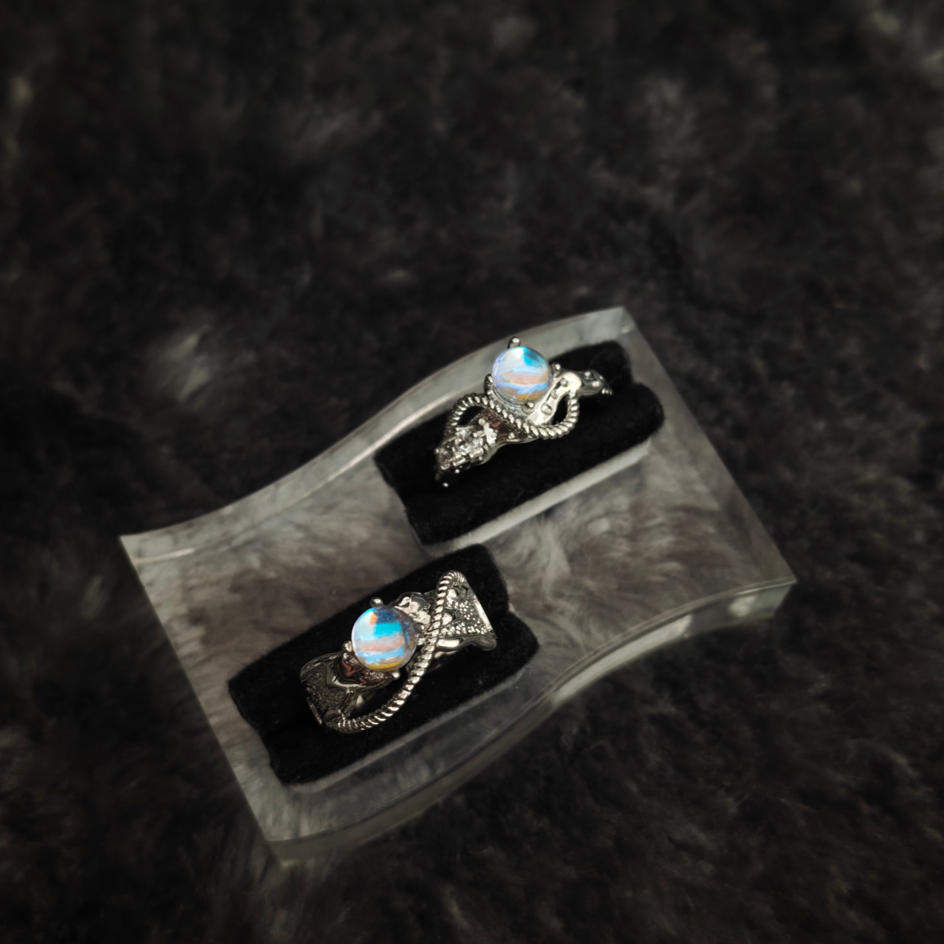 Two silver rings with iridescent cabochon on clear acrylic display stand, angled side view