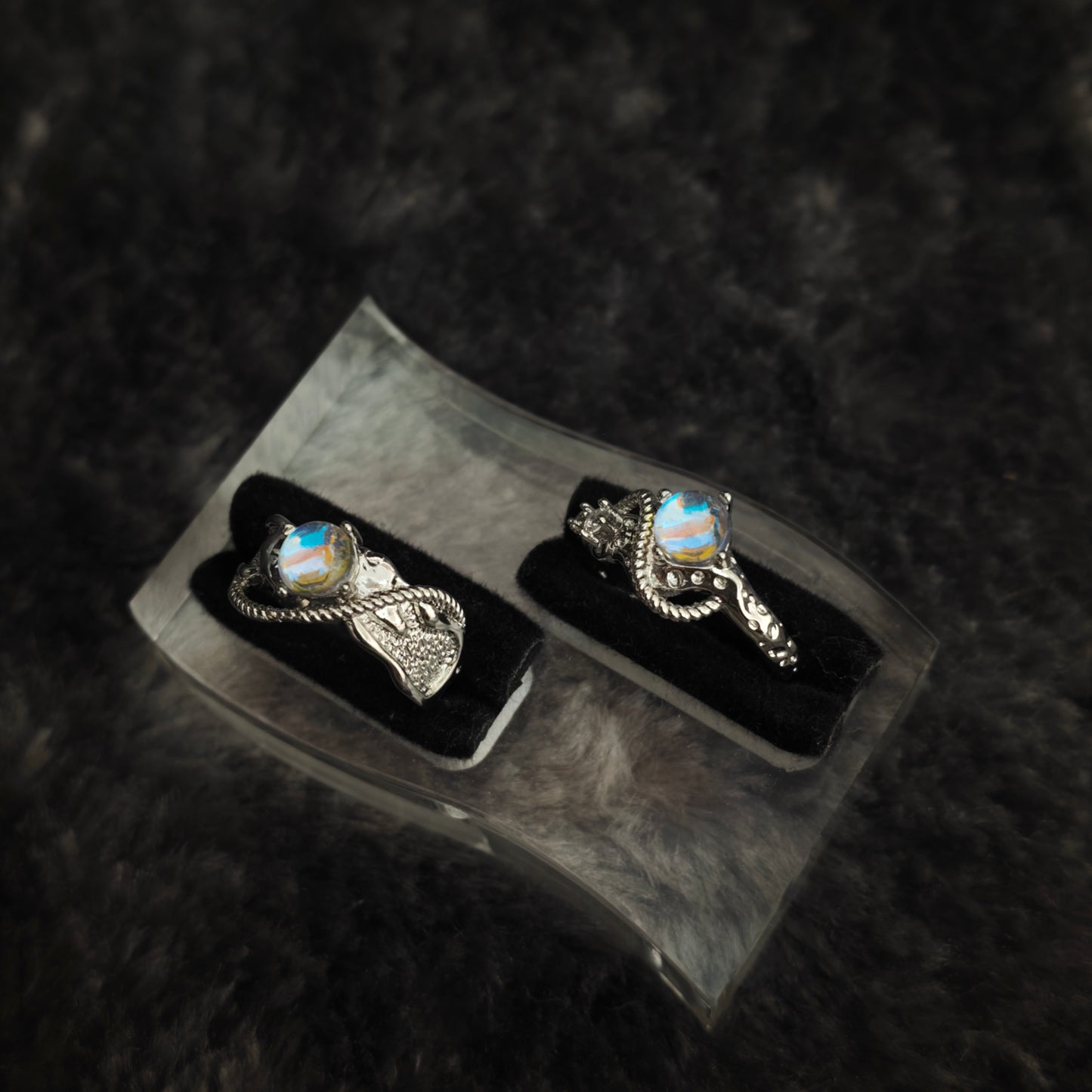 Silver arc ring set with iridescent stones displayed side by side on black velvet, close-up view