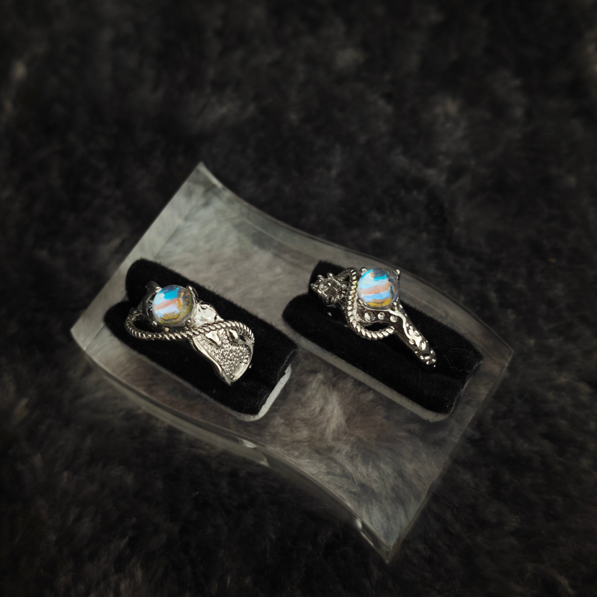 Silver arc ring set with iridescent stones displayed side by side on black velvet, close-up view