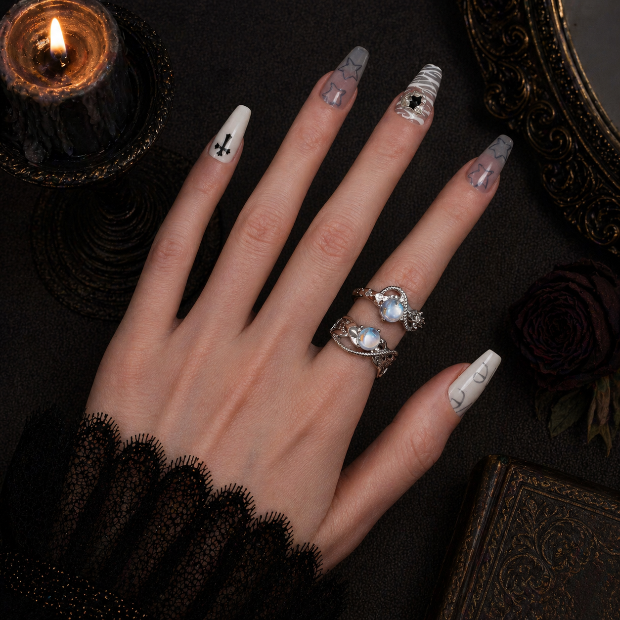 Hand with decorated nails and rings on a dark background with a candle and roses.