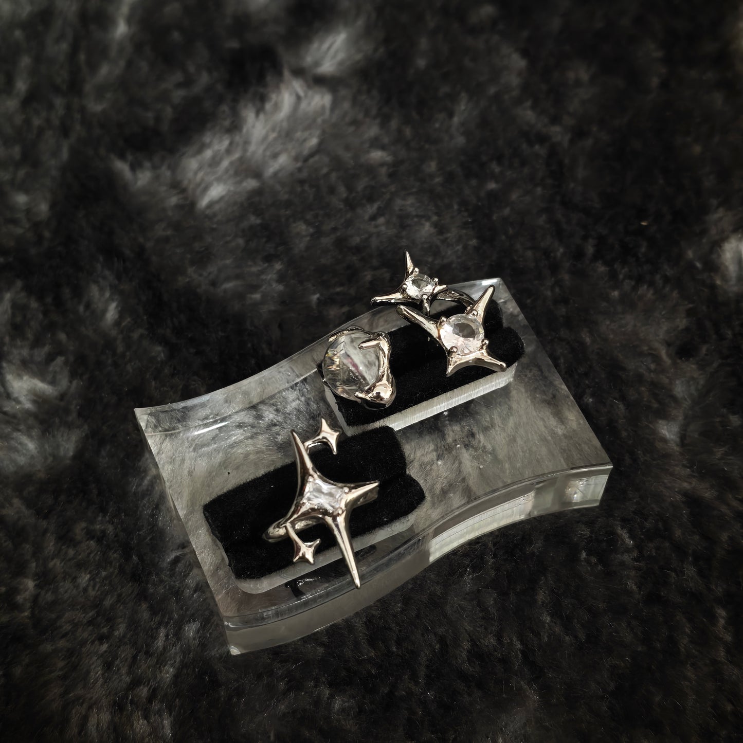 Two silver star spike rings with clear stones on clear acrylic display stand, angled overhead view