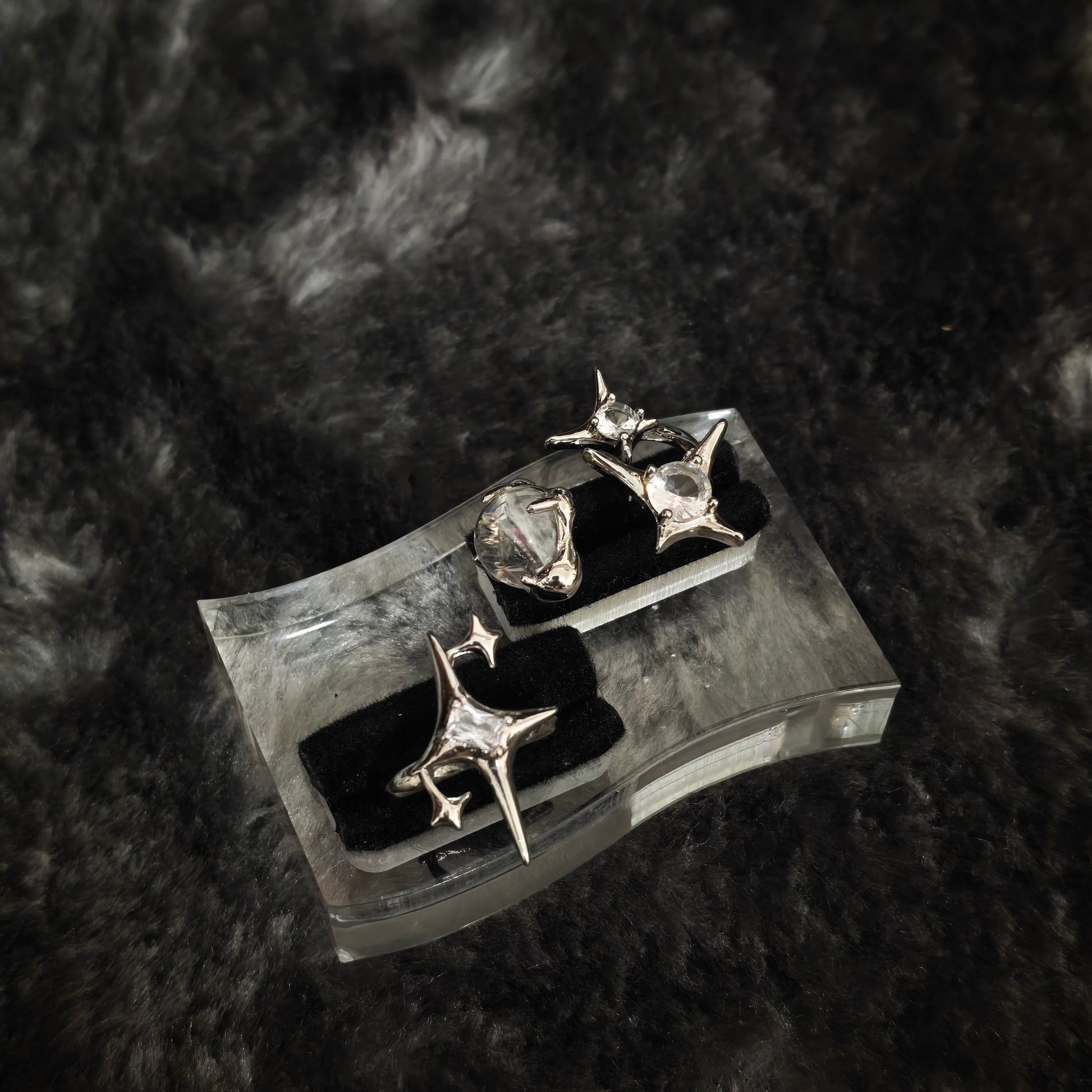 Two silver star spike rings with clear stones on clear acrylic display stand, angled overhead view