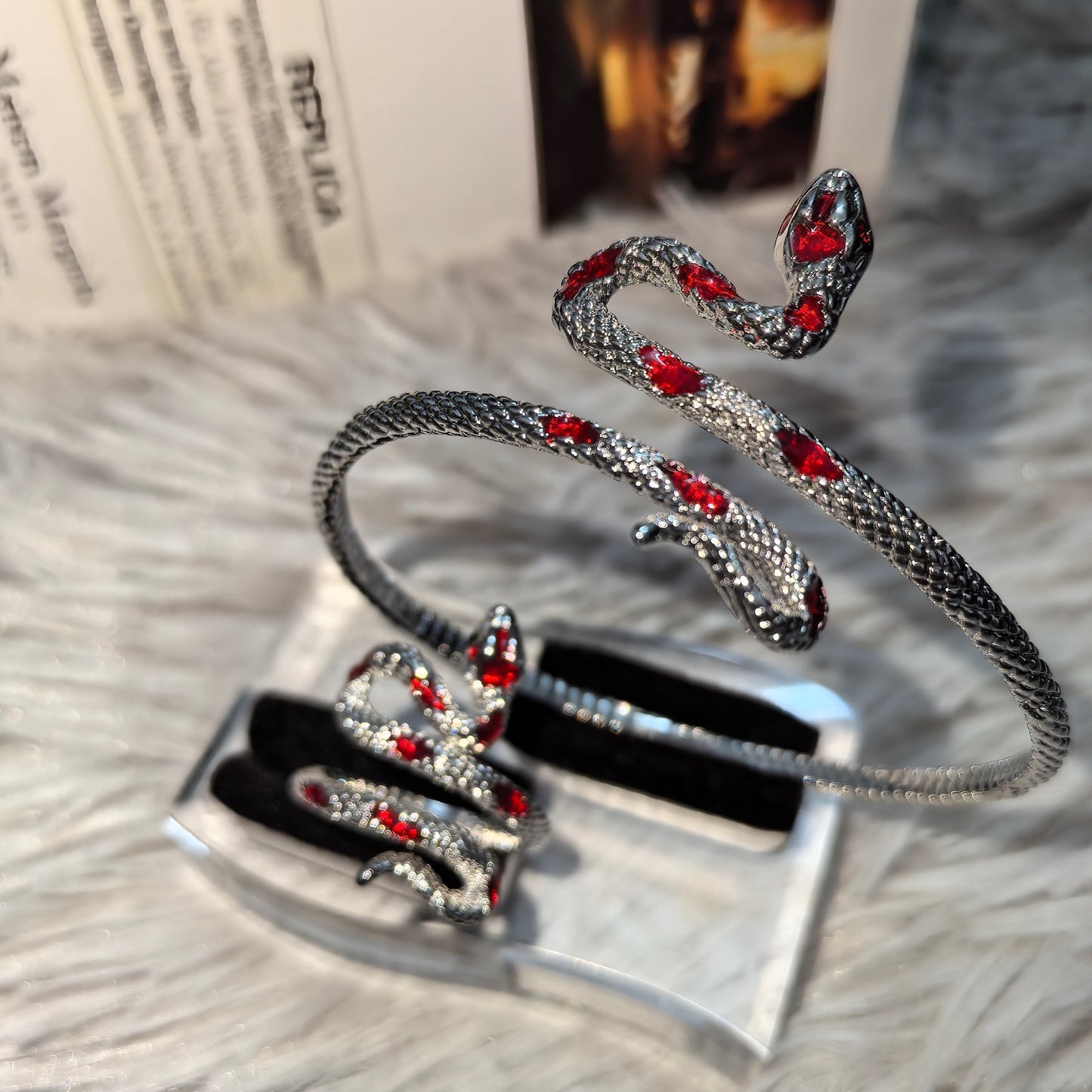 Silver snake-shaped bracelet with red stones on a textured surface