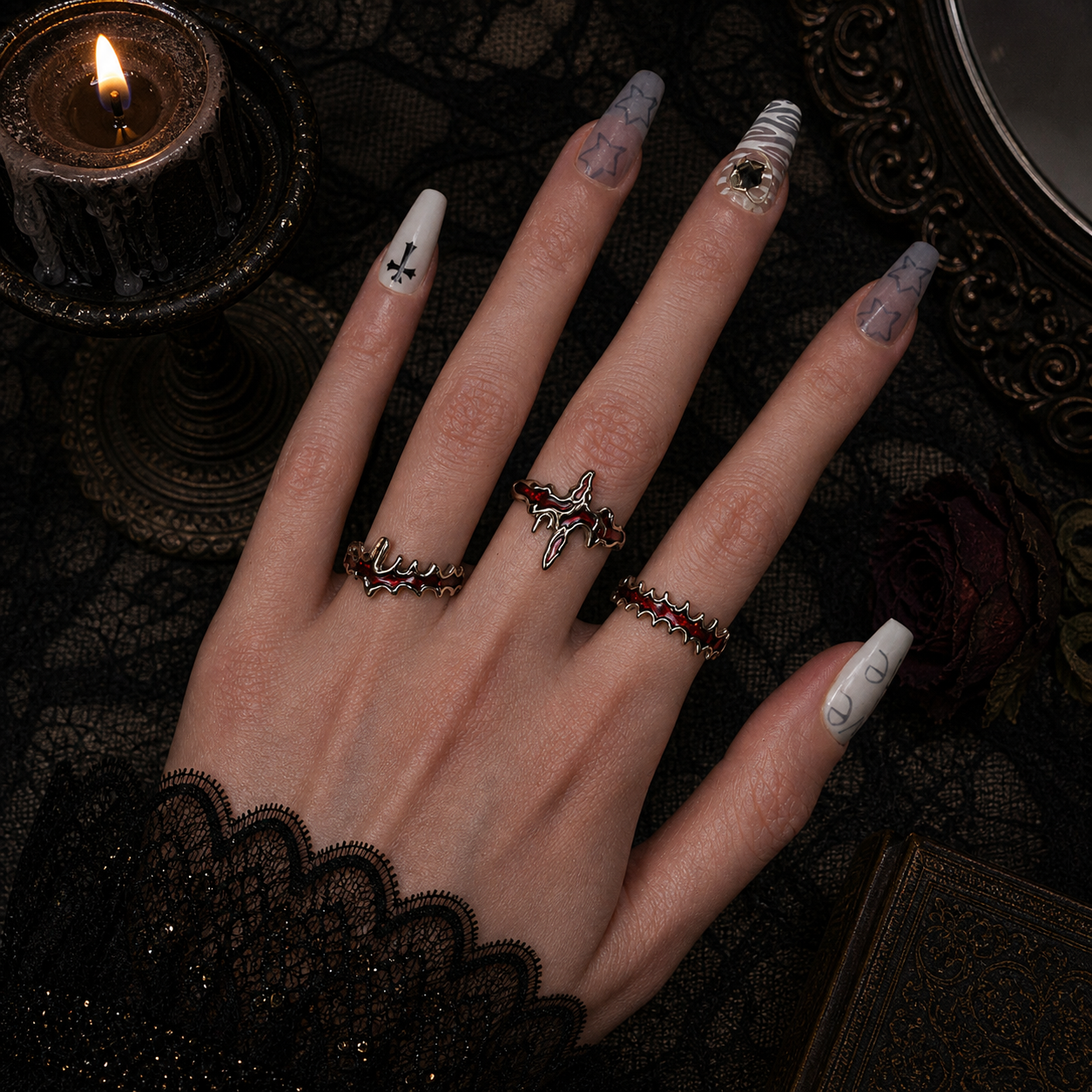 Three red enamel blood drip rings worn stacked on hand, dark gothic lace background with black candle