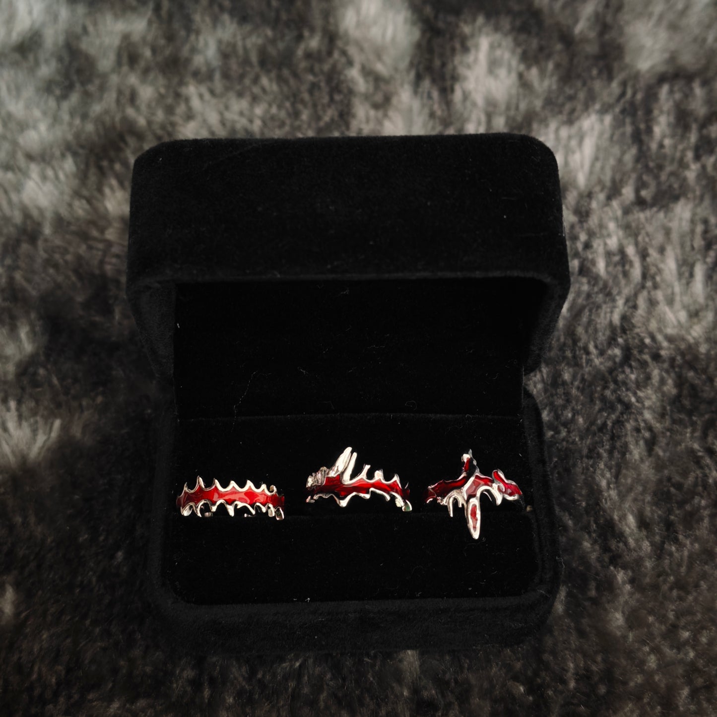 Three red enamel jagged rings on black mannequin hand showing fang band, dripping cross and blood drip band detail