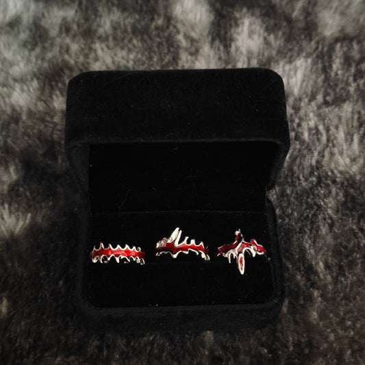 Three red enamel jagged rings on black mannequin hand showing fang band, dripping cross and blood drip band detail