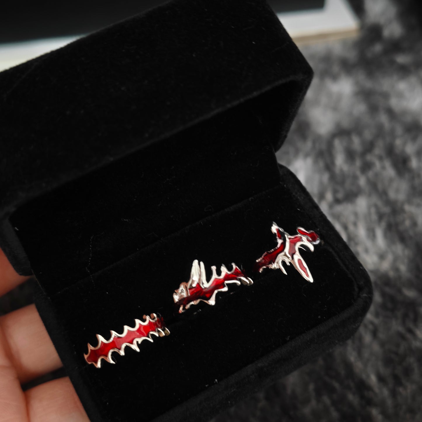 Three red enamel blood drip rings in open black velvet jewelry box, angled view