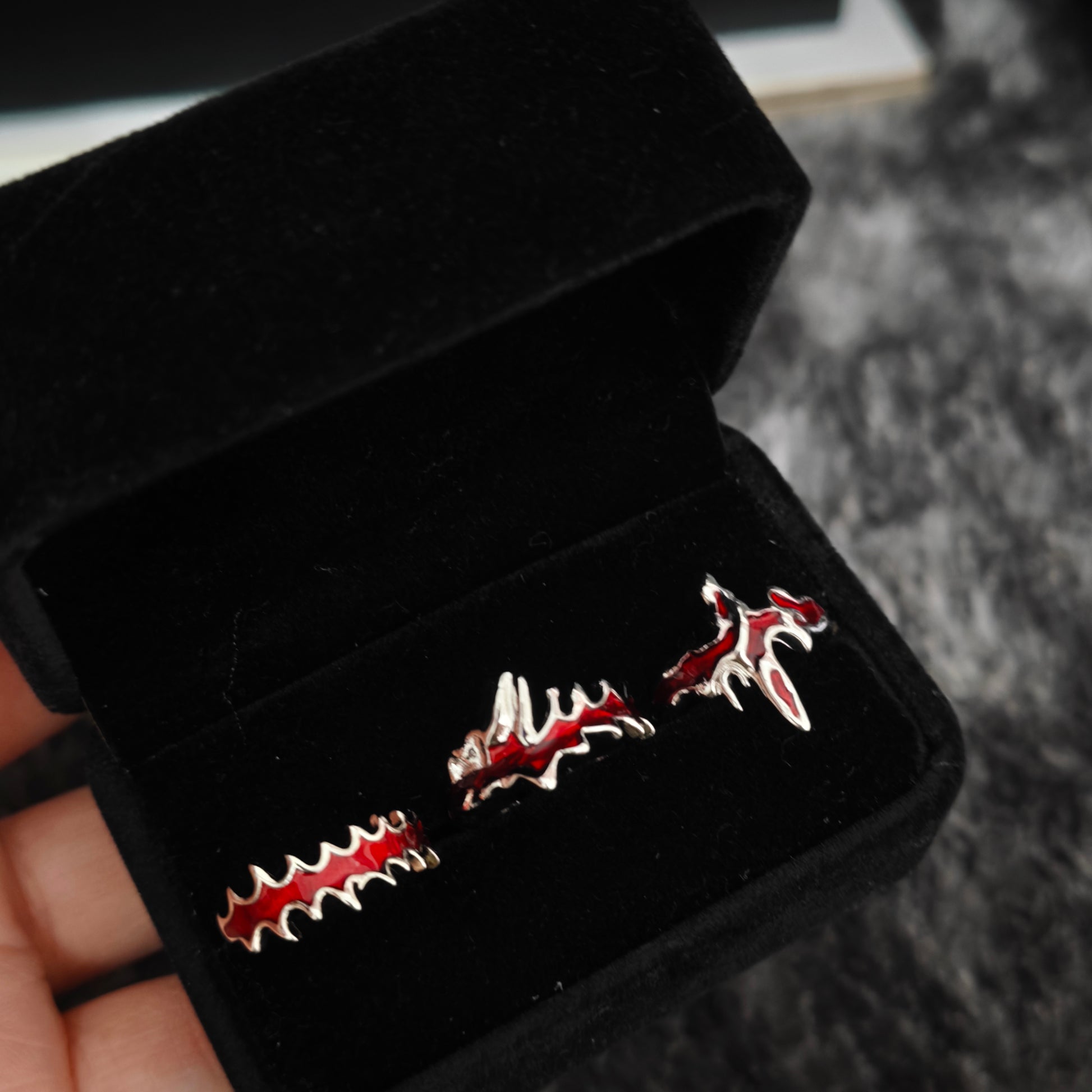 Three red enamel blood drip rings in open black velvet jewelry box, angled view