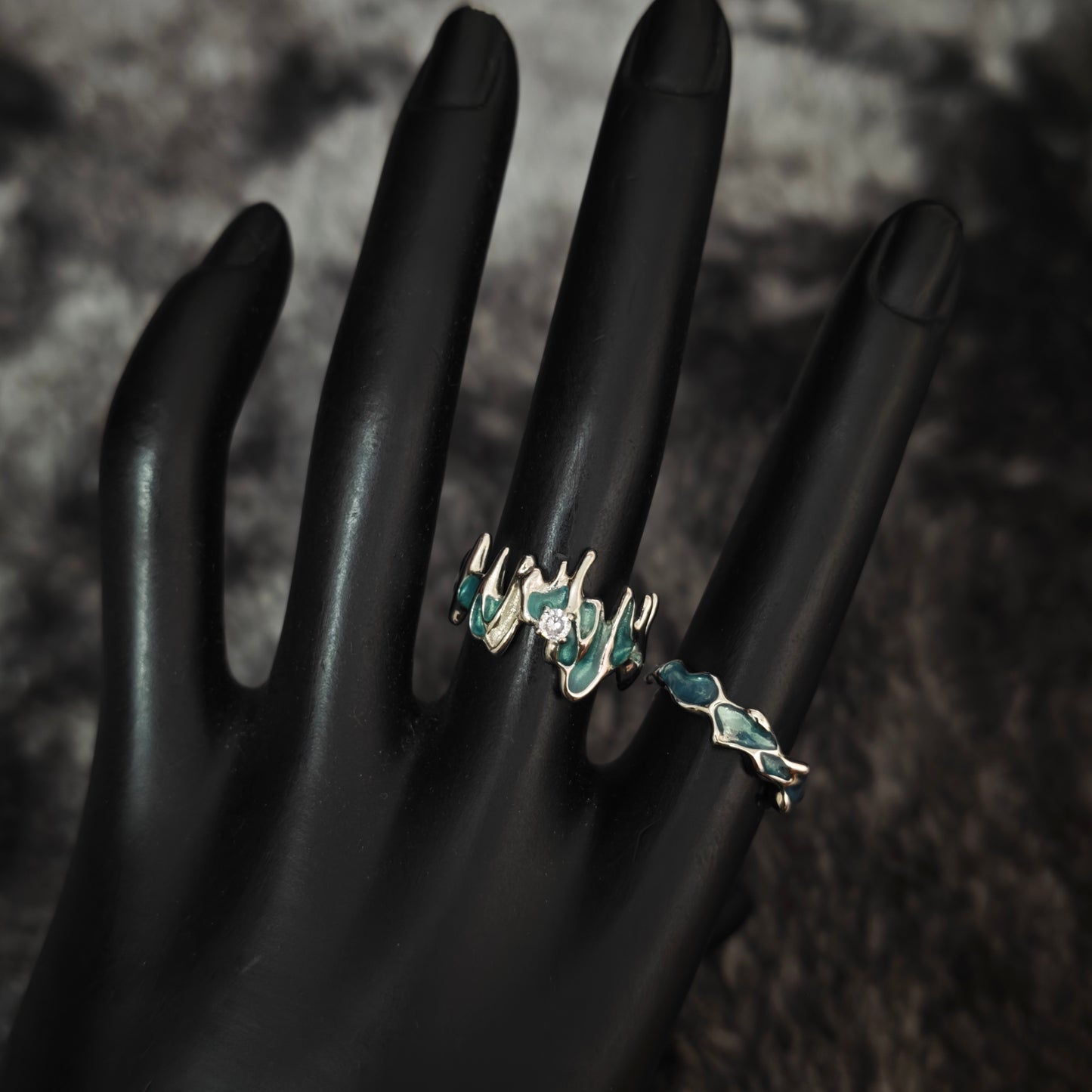 Teal enamel jagged molten ring with clear stone and slim teal wavy band on black mannequin hand, side view
